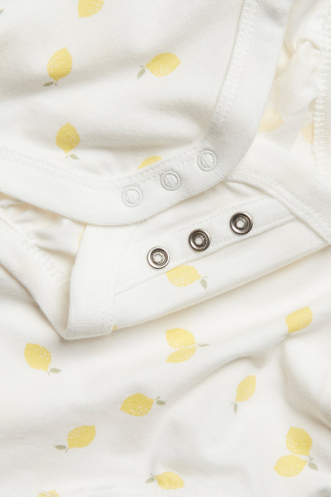 Närbild på en offwhite kortärmad babybody med gult citronmönster och tryckknappar.