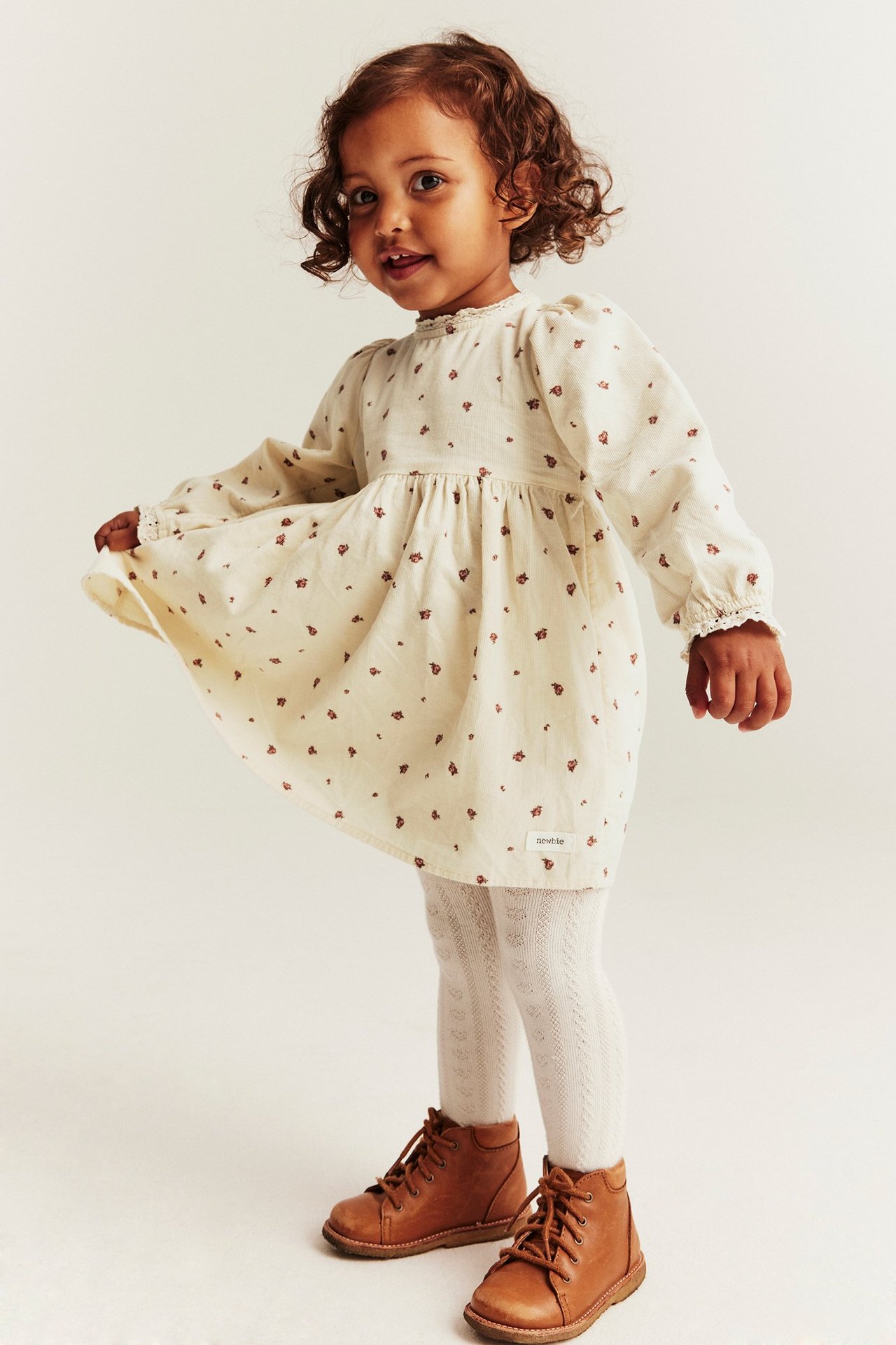 Lapsi: vaaleanbeige kukkavakosamettimekko pitsillä, valkoiset sukkahousut, ruskeat kengät.