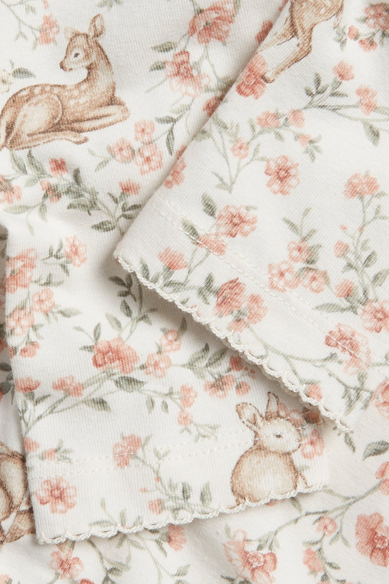 Zbliżenie na ecru bawełniane legginsy z kwiatowym wzorem, jelonkiem i królikiem, z wykończeniem picot.