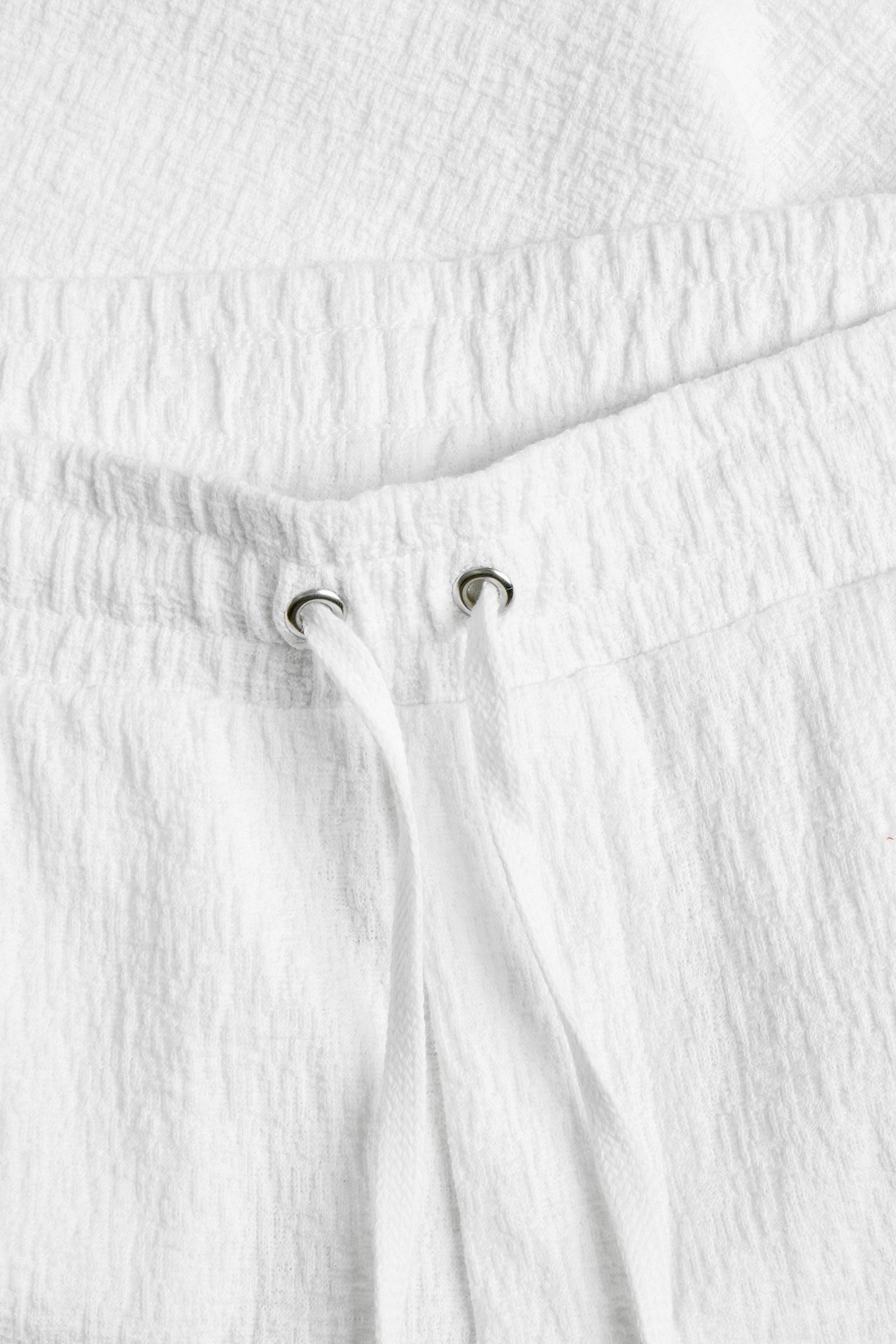 Zbliżenie na kremowe teksturowane szorty z elastycznym pasem i białym sznurkiem.