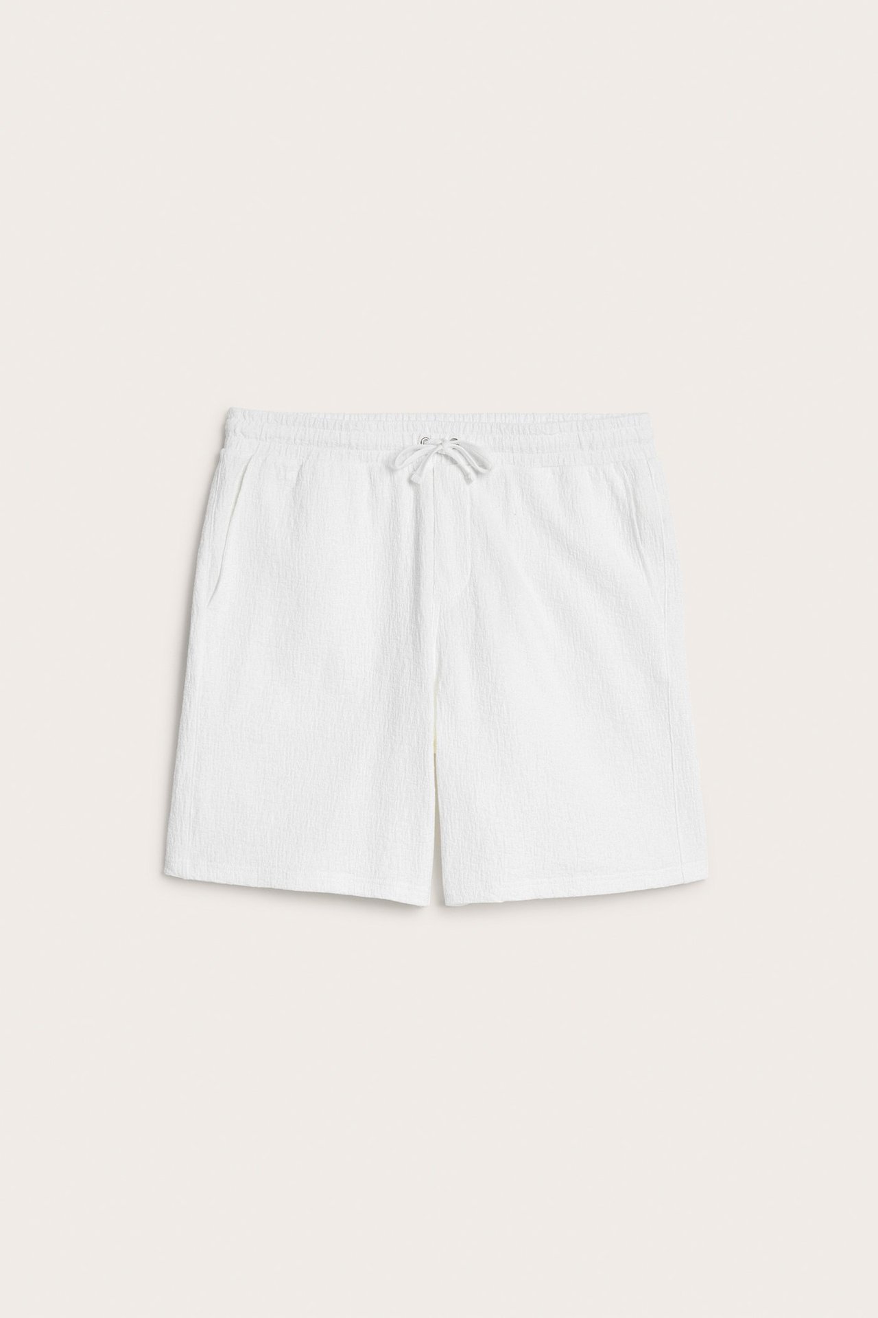 Edestä kuvatut luonnonvalkoiset strukturoidut shortsit, joissa joustava vyötärö ja kiristysnyöri.