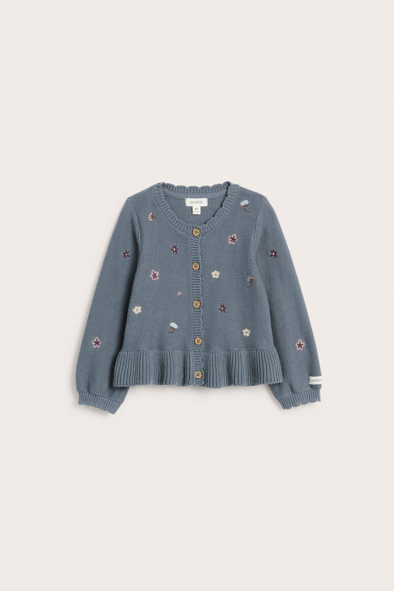 Widok z przodu niebieskiego dzianinowego sweterka bawełnianego dla dziecka z haftem kwiatowym, prążkowanymi brzegami i guzikami.
