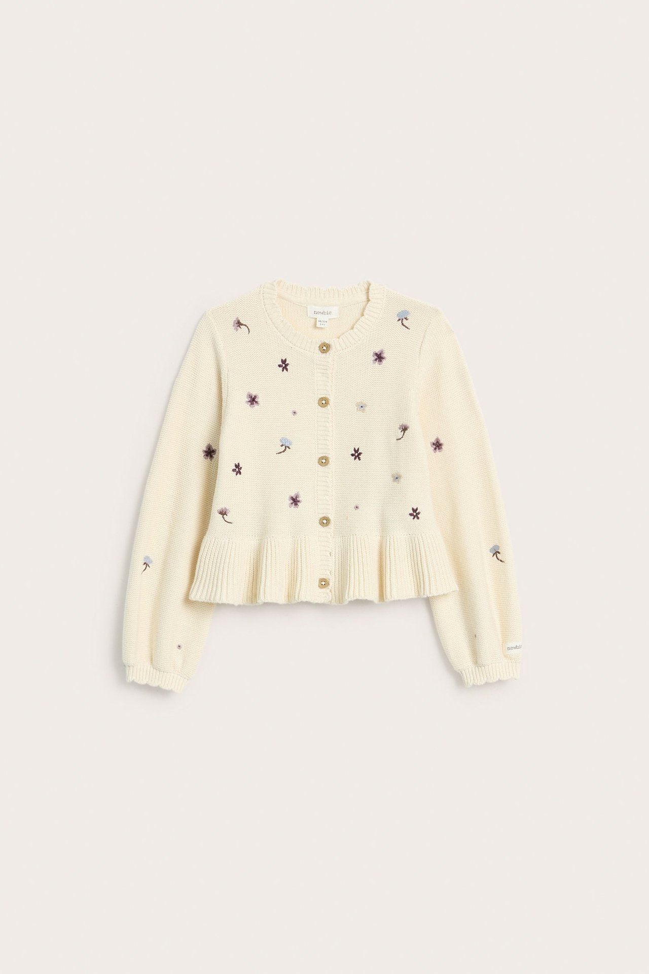 Edestä kuvattu vaaleanbeige puuvillaneuletakki lapsille, jossa kukkakirjontaa, uurretut reunat ja röyhelöhelma.