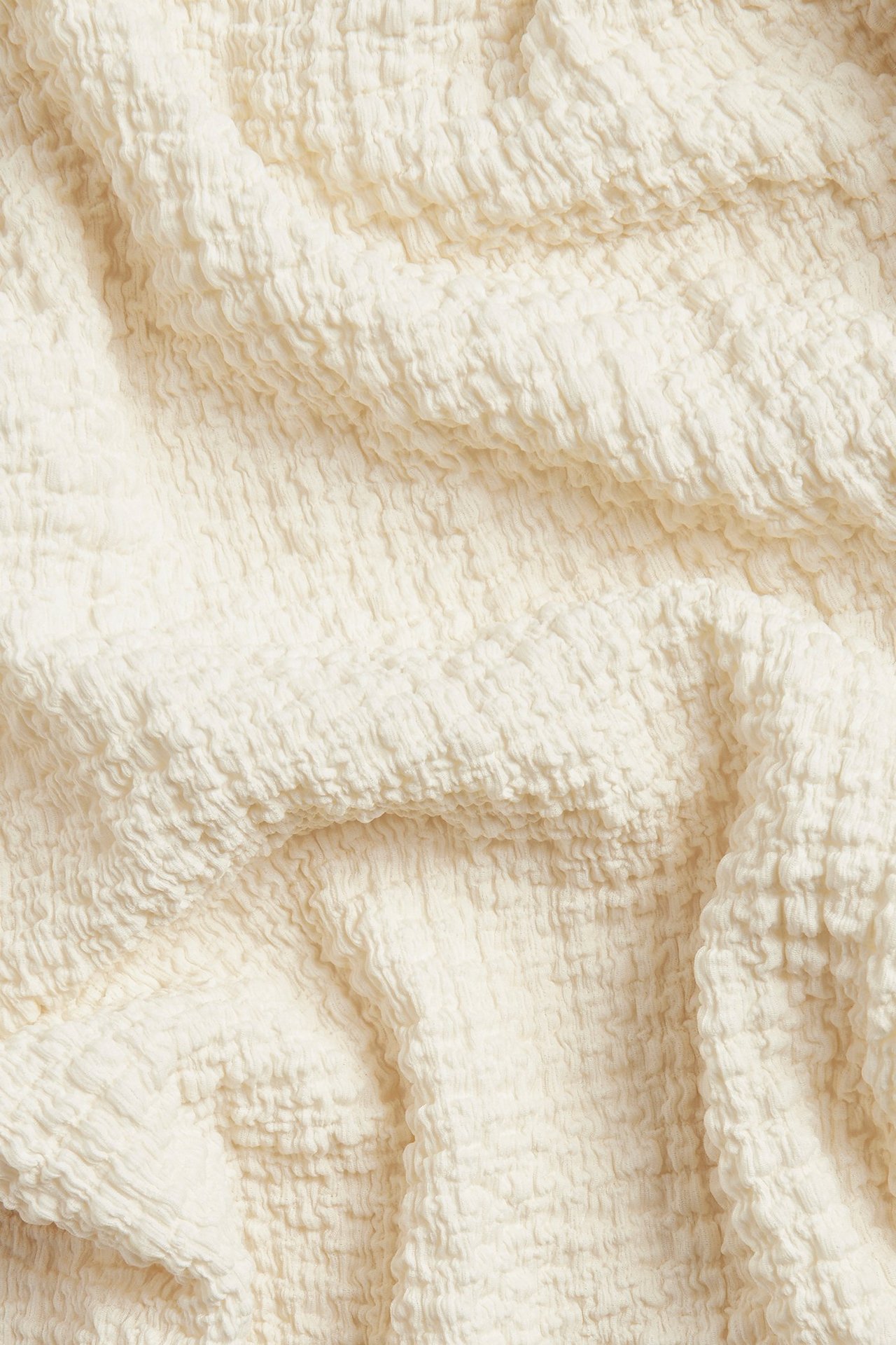 Zbliżenie na kremowy materiał z teksturowanym wzorem bąbelkowym.