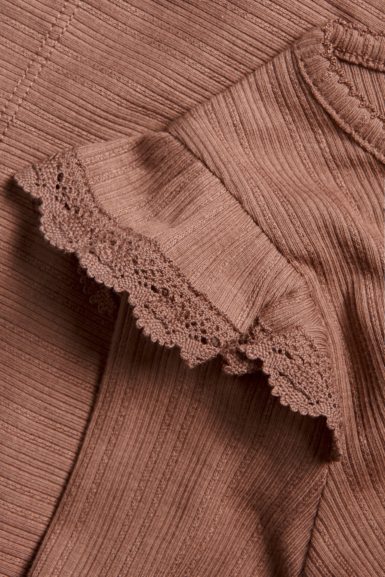Lähikuva tummanroosasta ribatusta pitkähihaisesta topista, jossa on röyhelöitä ja pitsireuna olkapäillä.