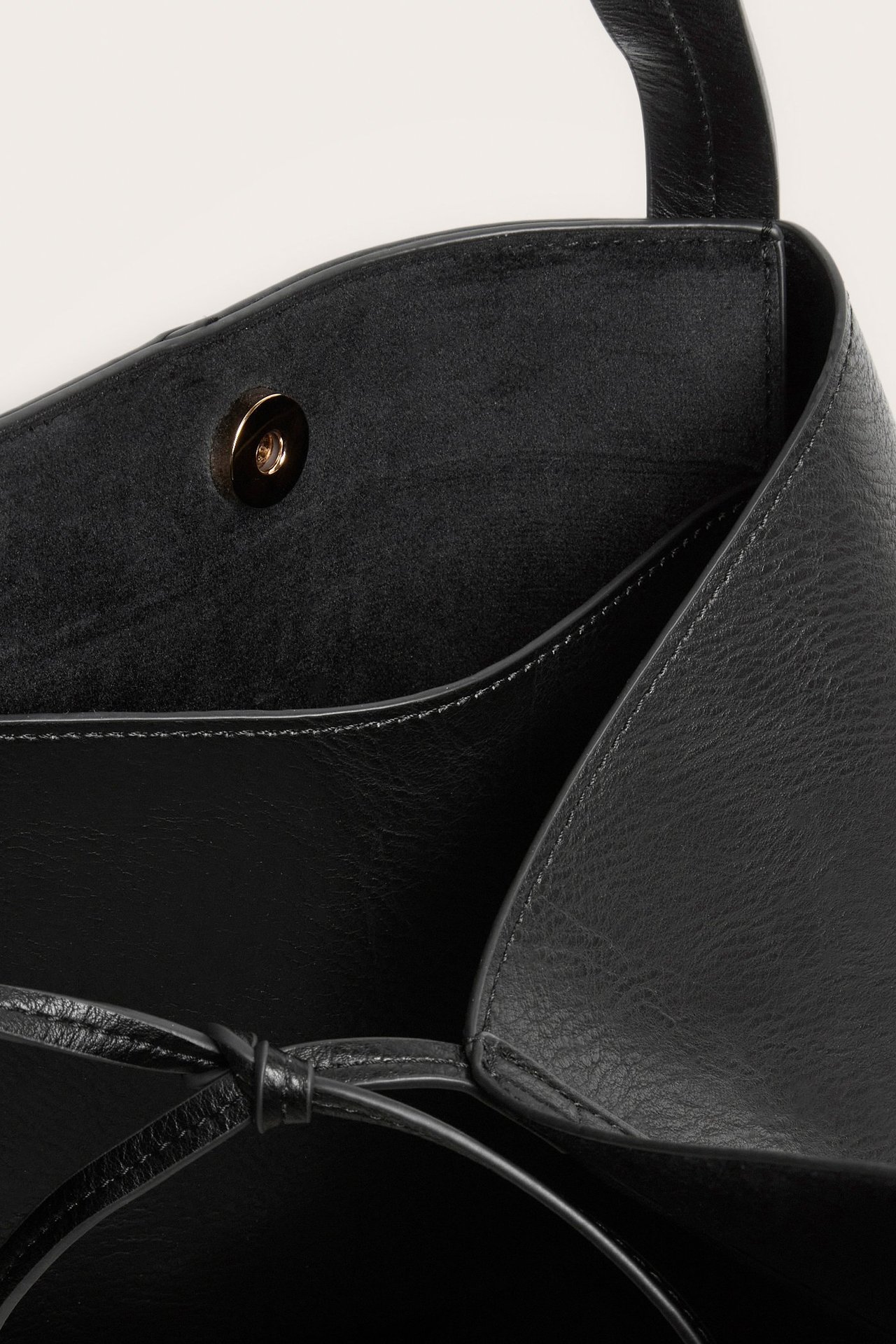 Zbliżenie wnętrza czarnej torby shopper ze sztucznej skóry, z zapięciem magnetycznym, kieszenią i związanymi paskami.