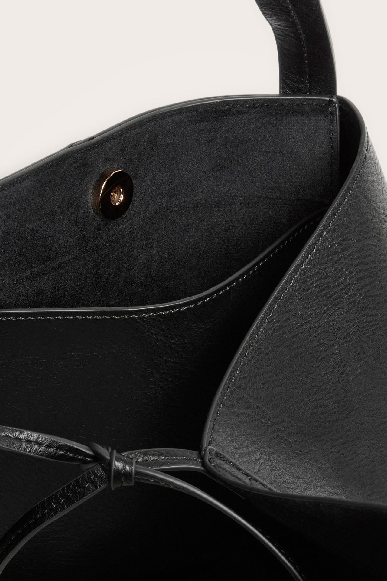 Nærbilde av innsiden av en svart skinn totebag med magnetisk trykknapp og knytedetalj.