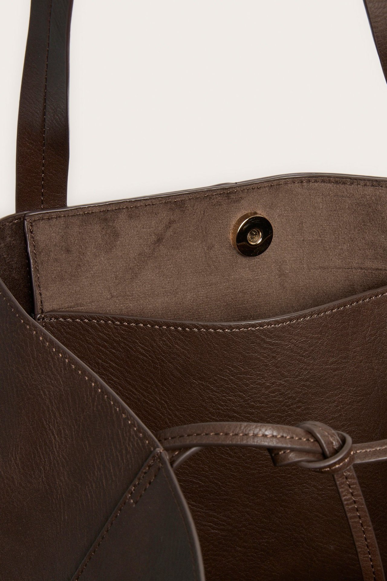 Nærbilde av en åpen mørkebrun totebag i imitert skinn med magnetlås og snørede sider.