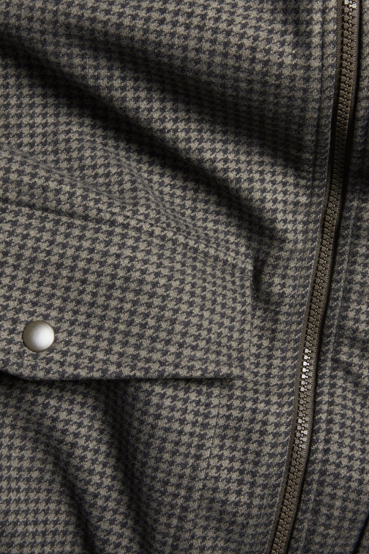 Zbliżenie brązowej kurtki w kratę z recyklingowanego poliestru, z zamkiem błyskawicznym i kieszenią na zatrzask.