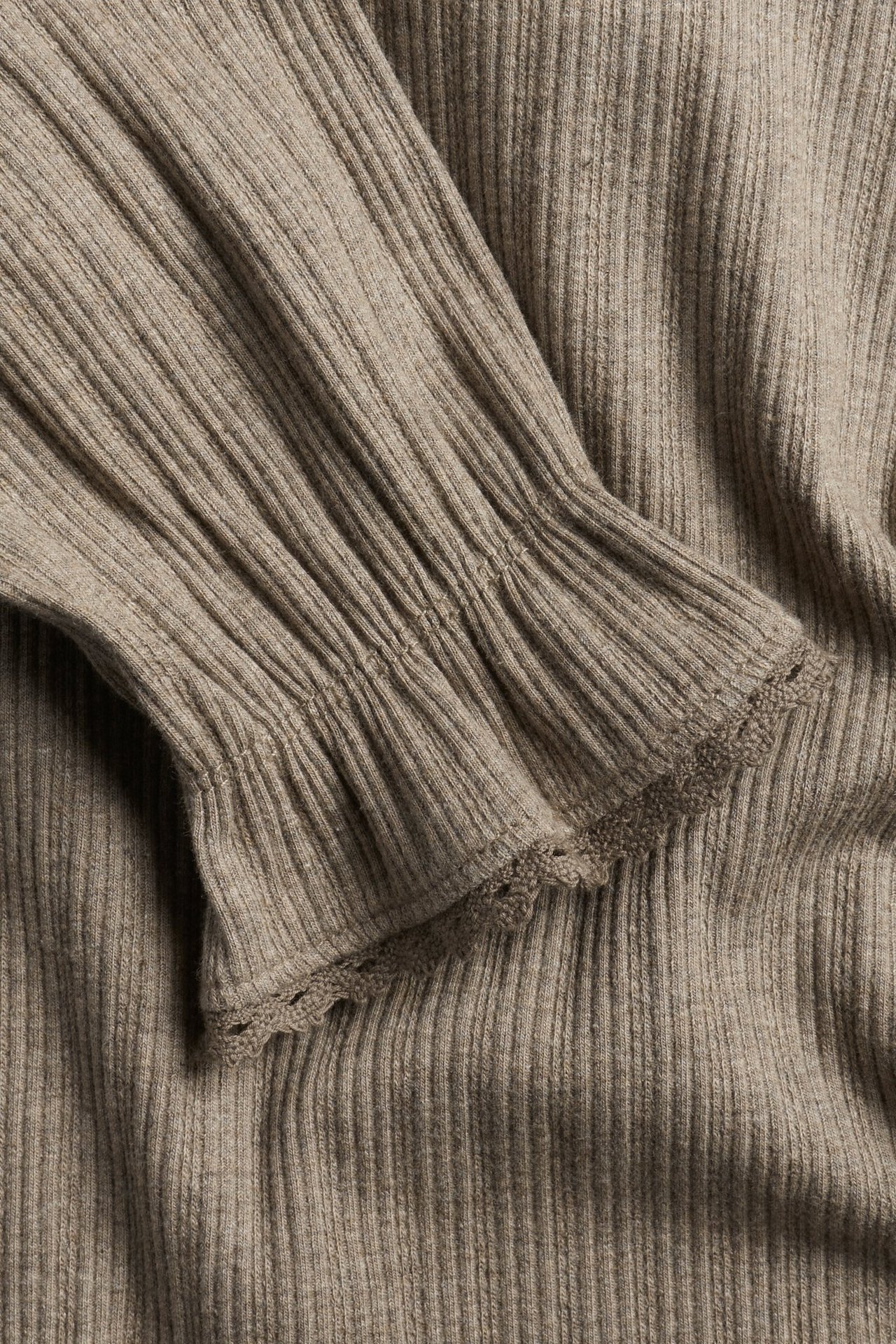 Zbliżenie brązowego melanżowego prążkowanego topu z falbanką i koronkowym brzegiem przy mankiecie.