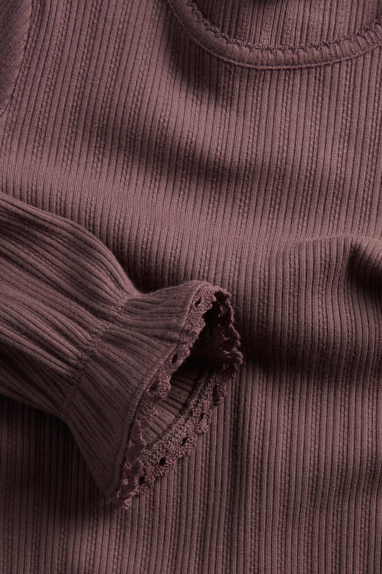 Zbliżenie liliowego prążkowanego topu z długim rękawem, falbankami i koronkowym wykończeniem.