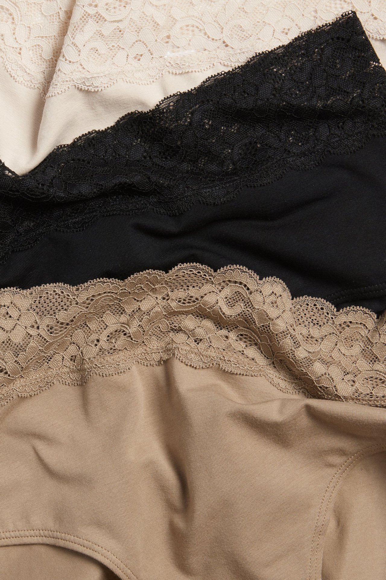 Zbliżenie trzech bawełnianych majtek typu mid brief z koronką: jasnobeżowe, czarne i średniobeżowe.