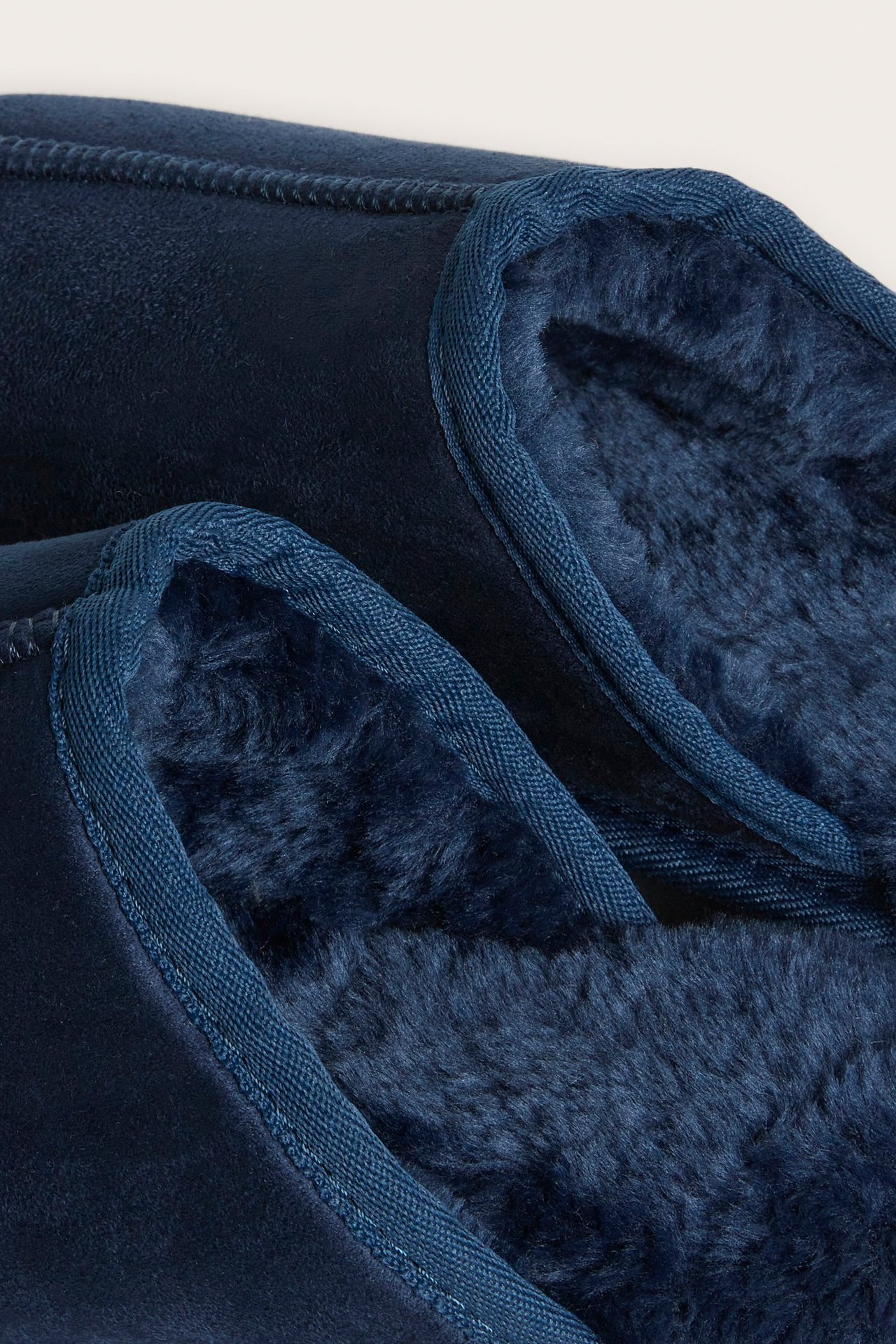 Zbliżenie na ciemnoniebieskie kapcie z imitacji zamszu z ciemnoniebieskim futerkiem i obszytymi brzegami.