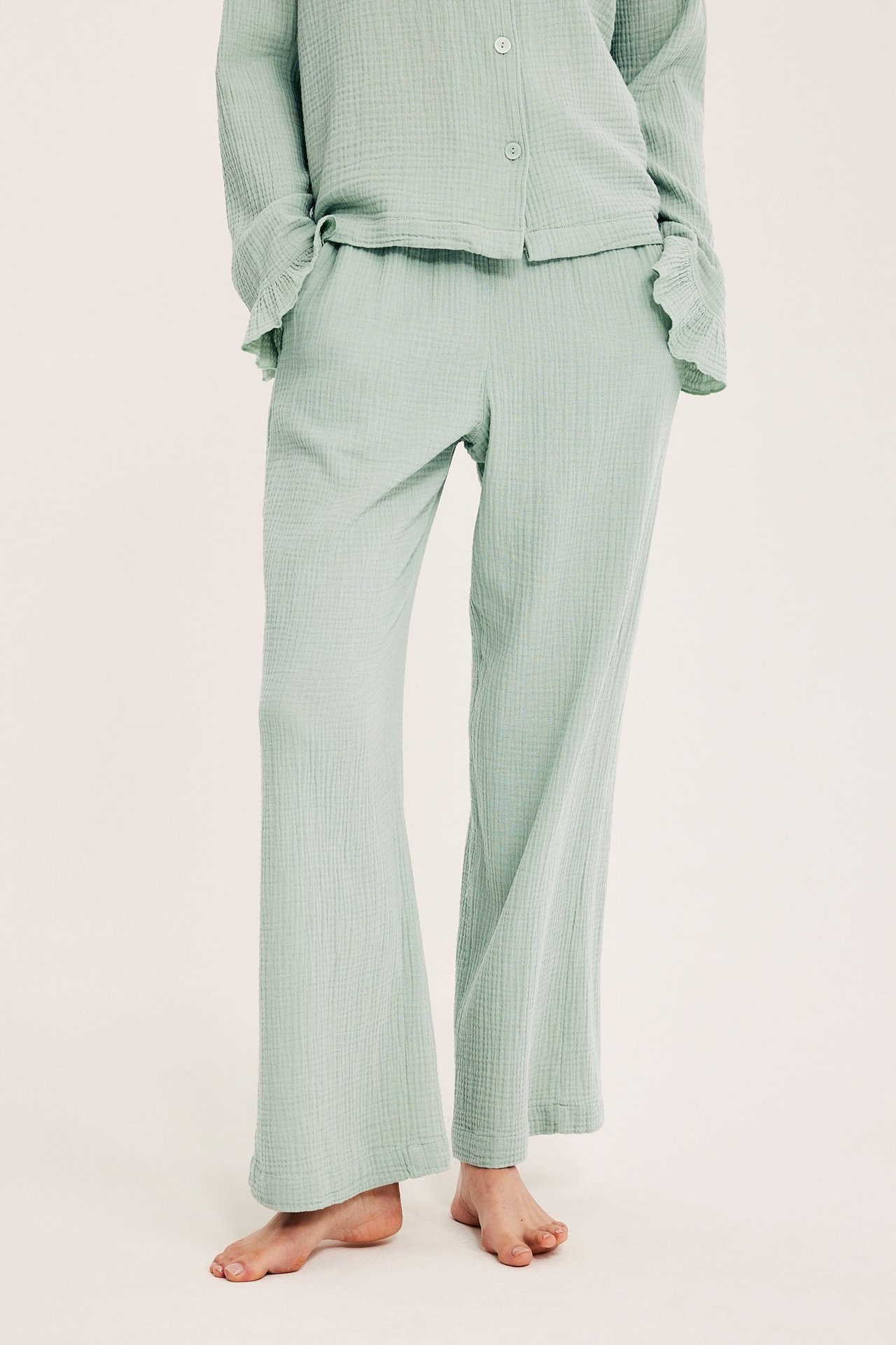 Edestä kuvattu nainen yllään vaaleanvihreät kuvioidut puuvillapyjamahousut ja yhteensopiva pyjamatoppi.