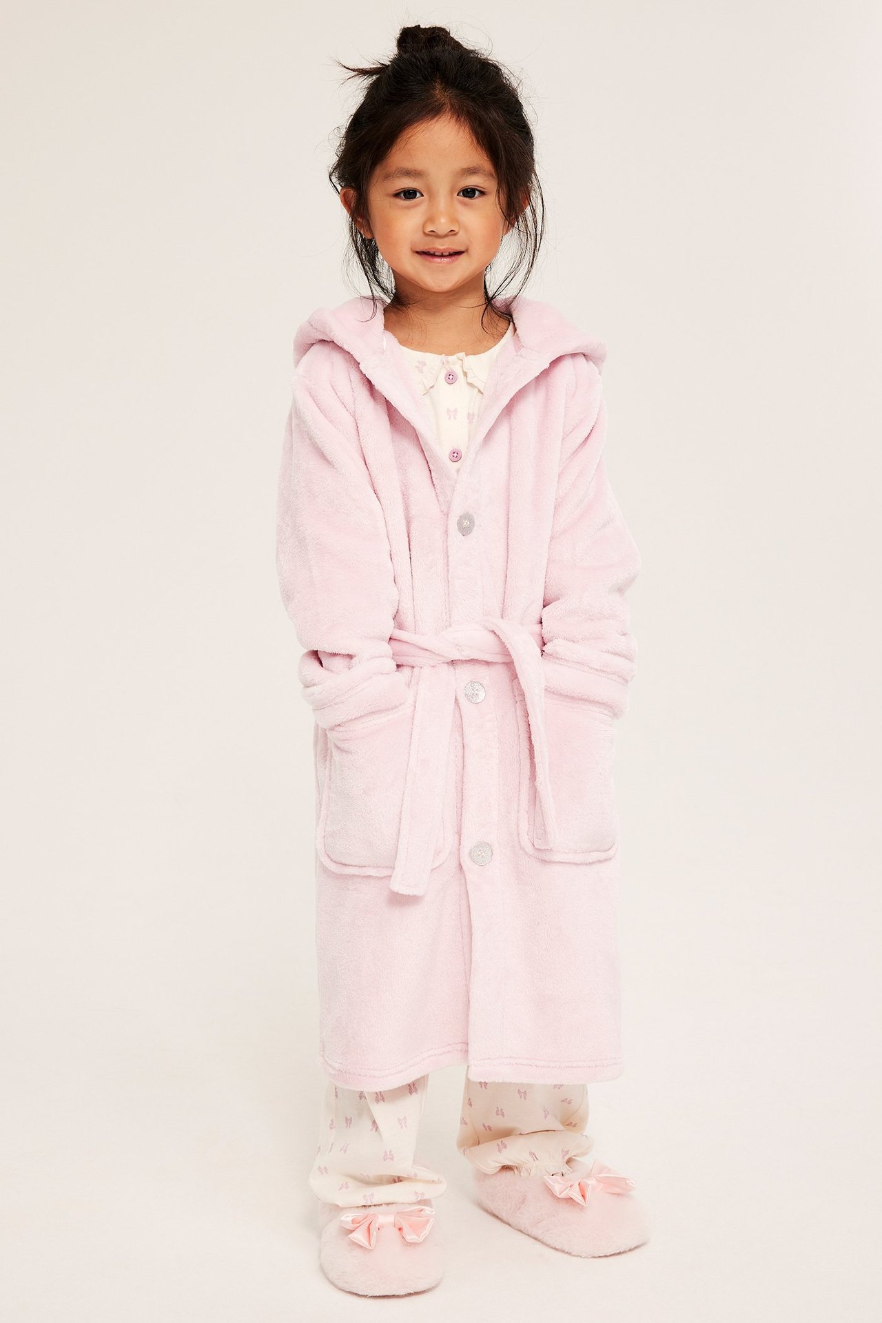 Edestäpäin, lapsi vaaleanpunaisessa fleece-yksisarviskylpytakissa, pyjaman päällä, vaaleanpunaiset tossut jalassa.