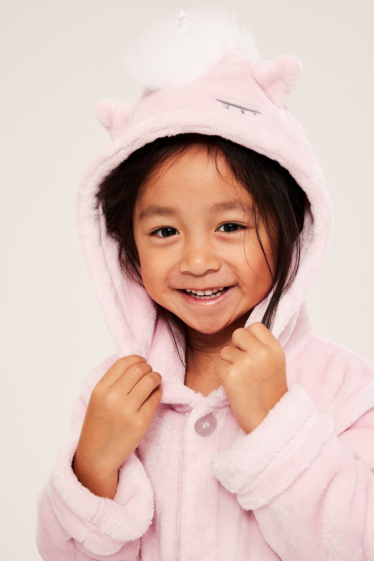 Zbliżenie, uśmiechnięte dziecko w różowym, polarowym szlafroku jednorożca z kapturem i guzikiem.