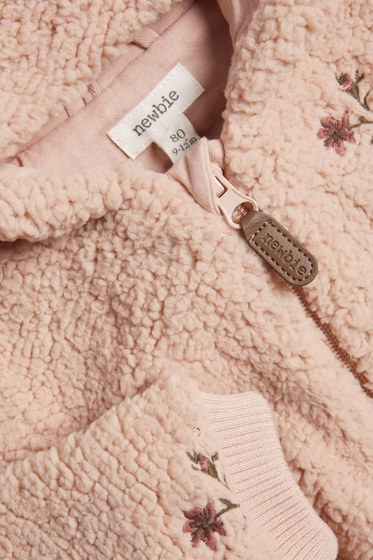 Zbliżenie różowej kurtki polarowej z haftem kwiatowym, pełnym zamkiem błyskawicznym i ściągaczami.