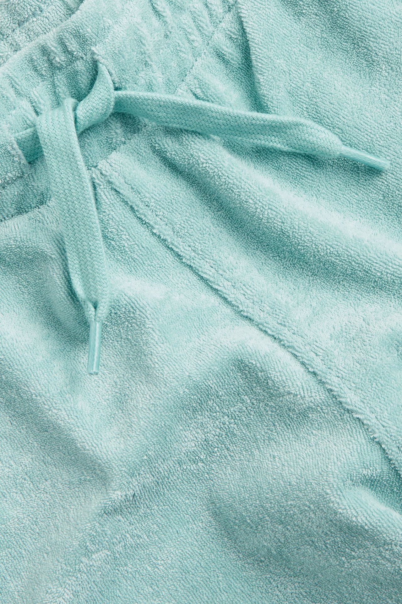 Zbliżenie na jasnozielone szorty frotte, ukazujące miękką fakturę materiału i zawiązany sznurek.