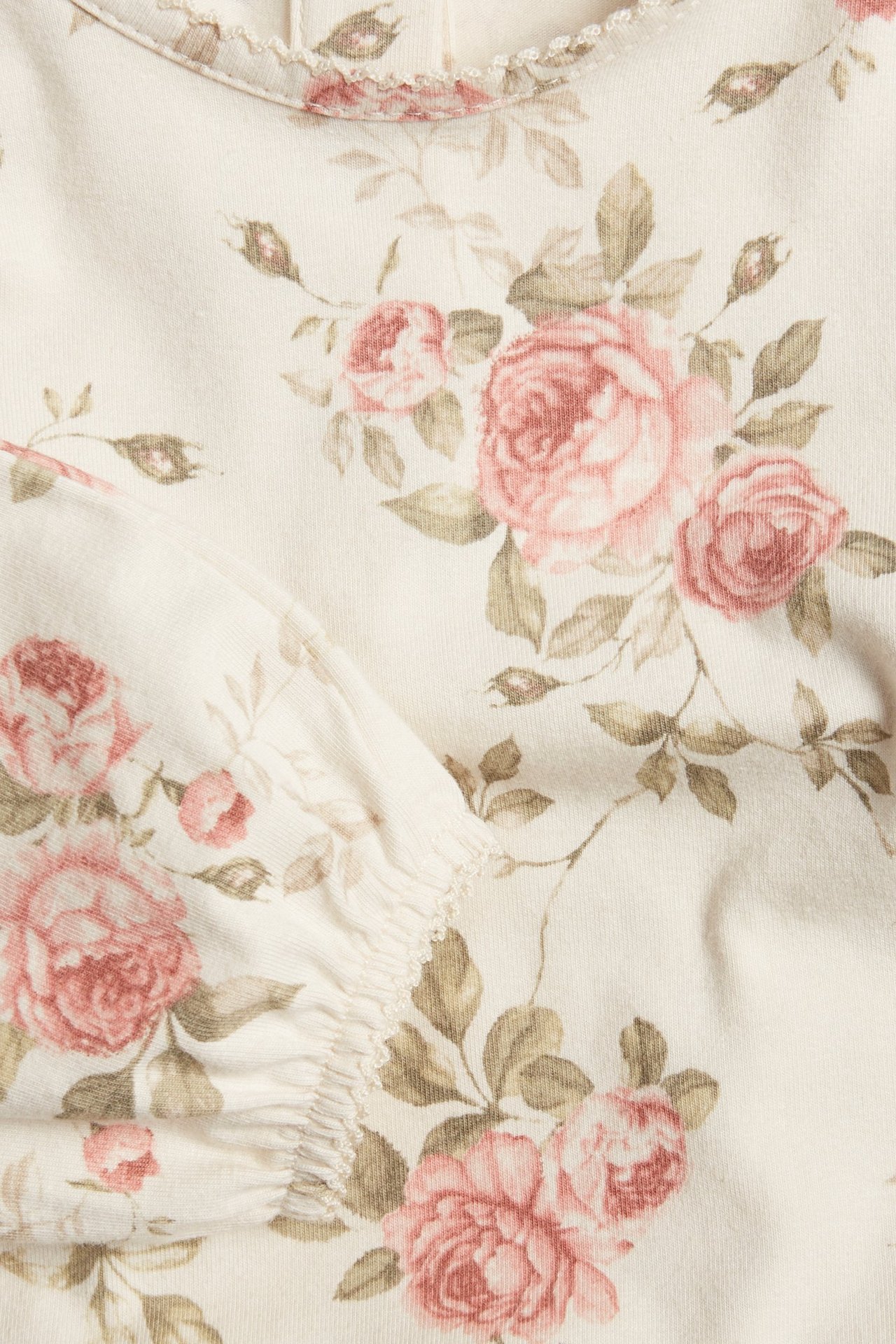 Zbliżenie na jasnobeżowe body niemowlęce z różowym kwiatowym wzorem, picot i bufiastym rękawem.