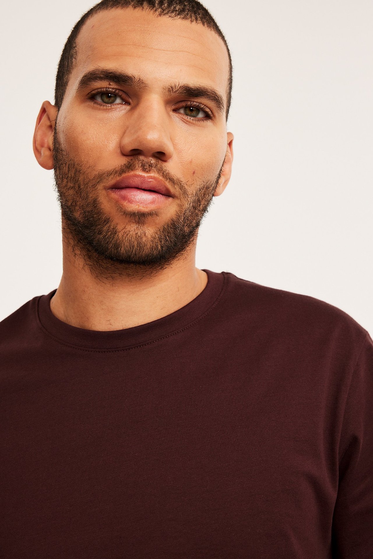 Lähikuva edestä miehestä, jolla on yksivärinen viininpunainen pyöreäkauluksinen puuvillainen t-paita.