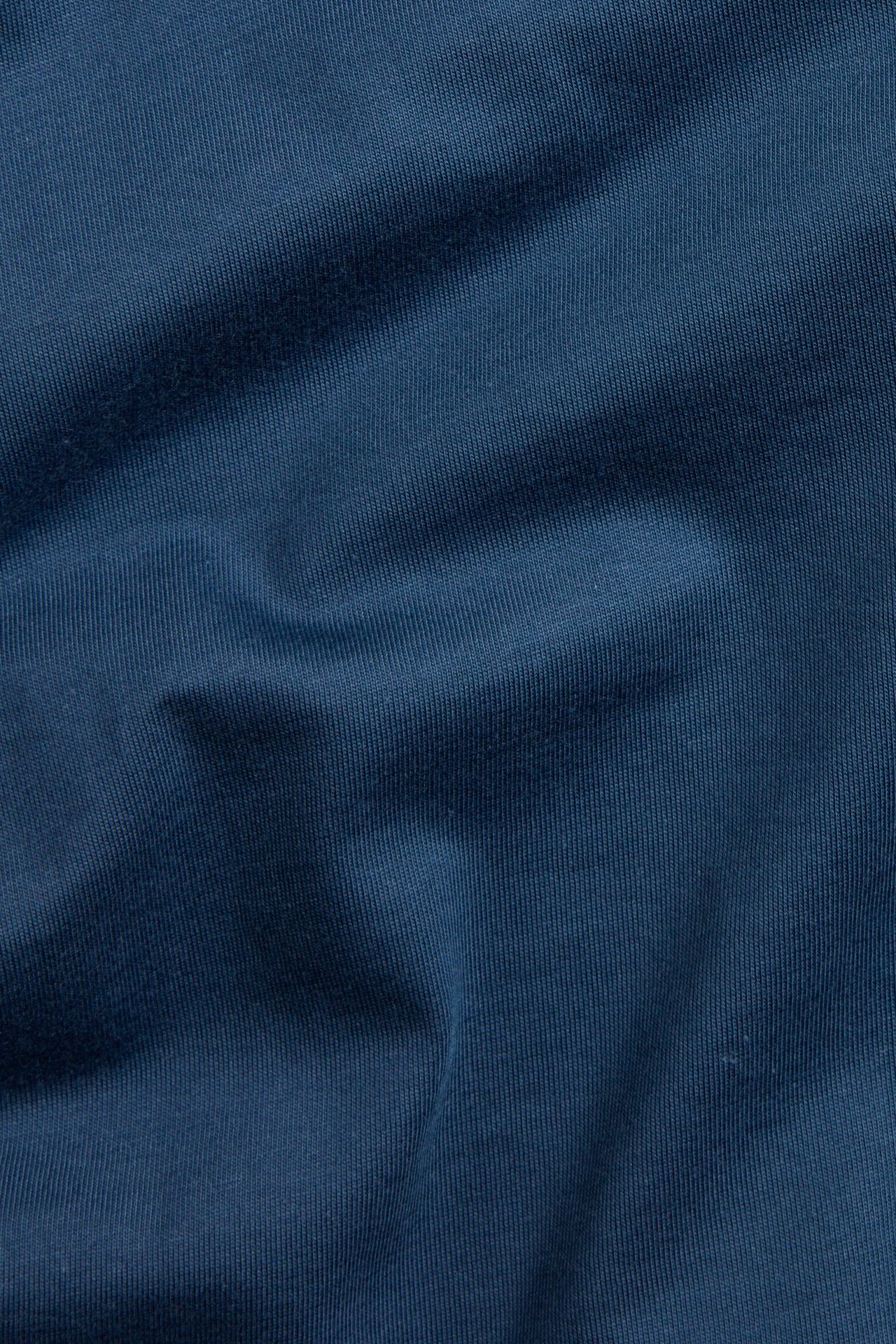 Zbliżenie na jednolity niebieski materiał bawełnianej koszulki z delikatnymi zagnieceniami.