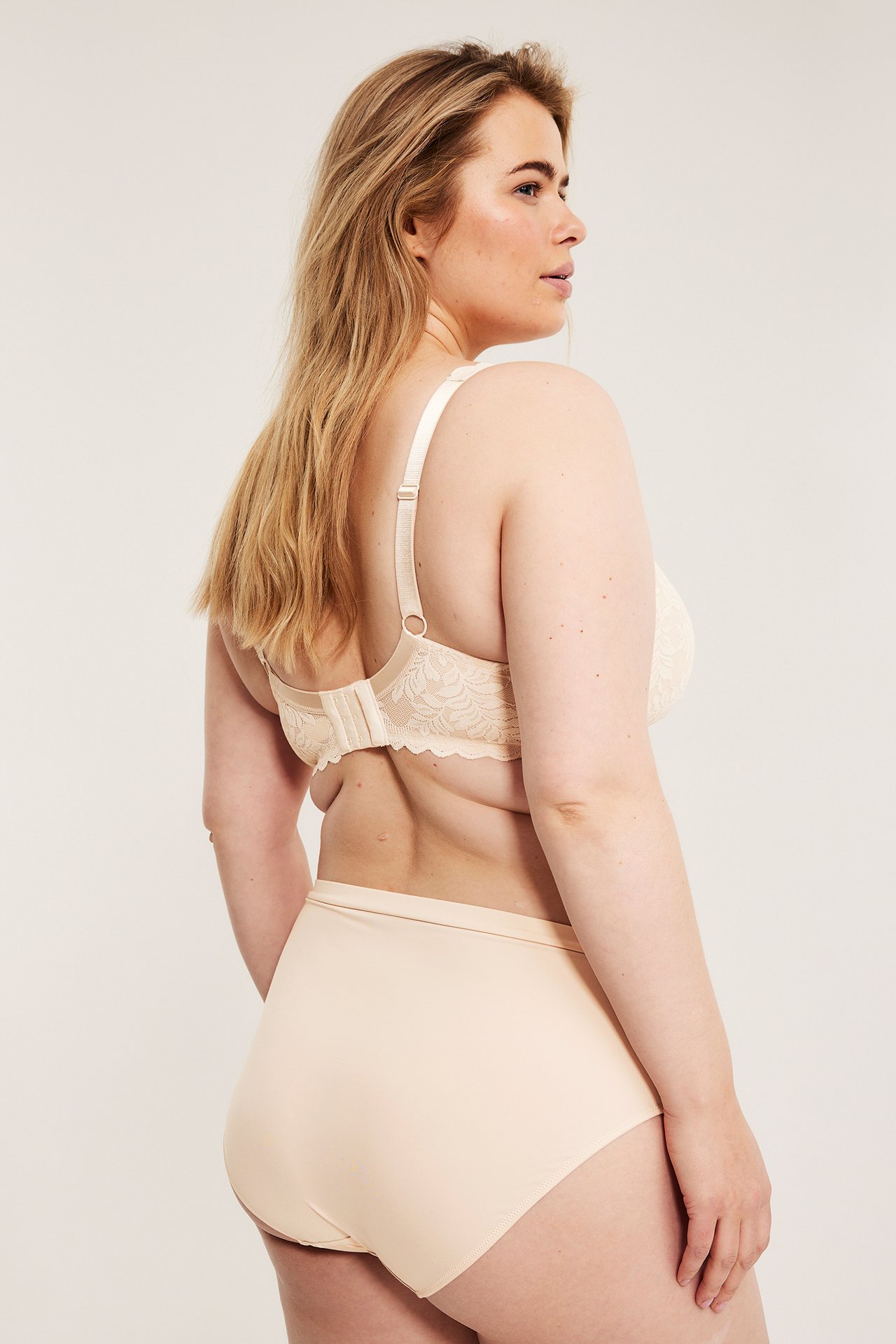 Bak/sidovy av en kvinna i ljusrosa micro-brieftrosa med resår och matchande ljusrosa spets-BH.