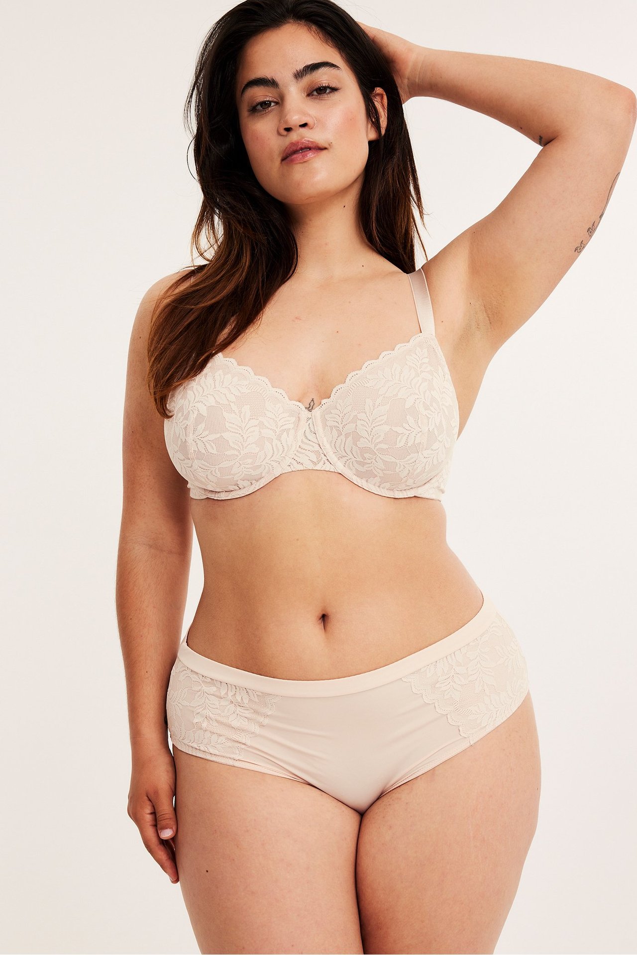 Frontbilde av en kvinne i lys rosa mikro-briefs med blondeapplikasjoner og matchende blonde-BH.