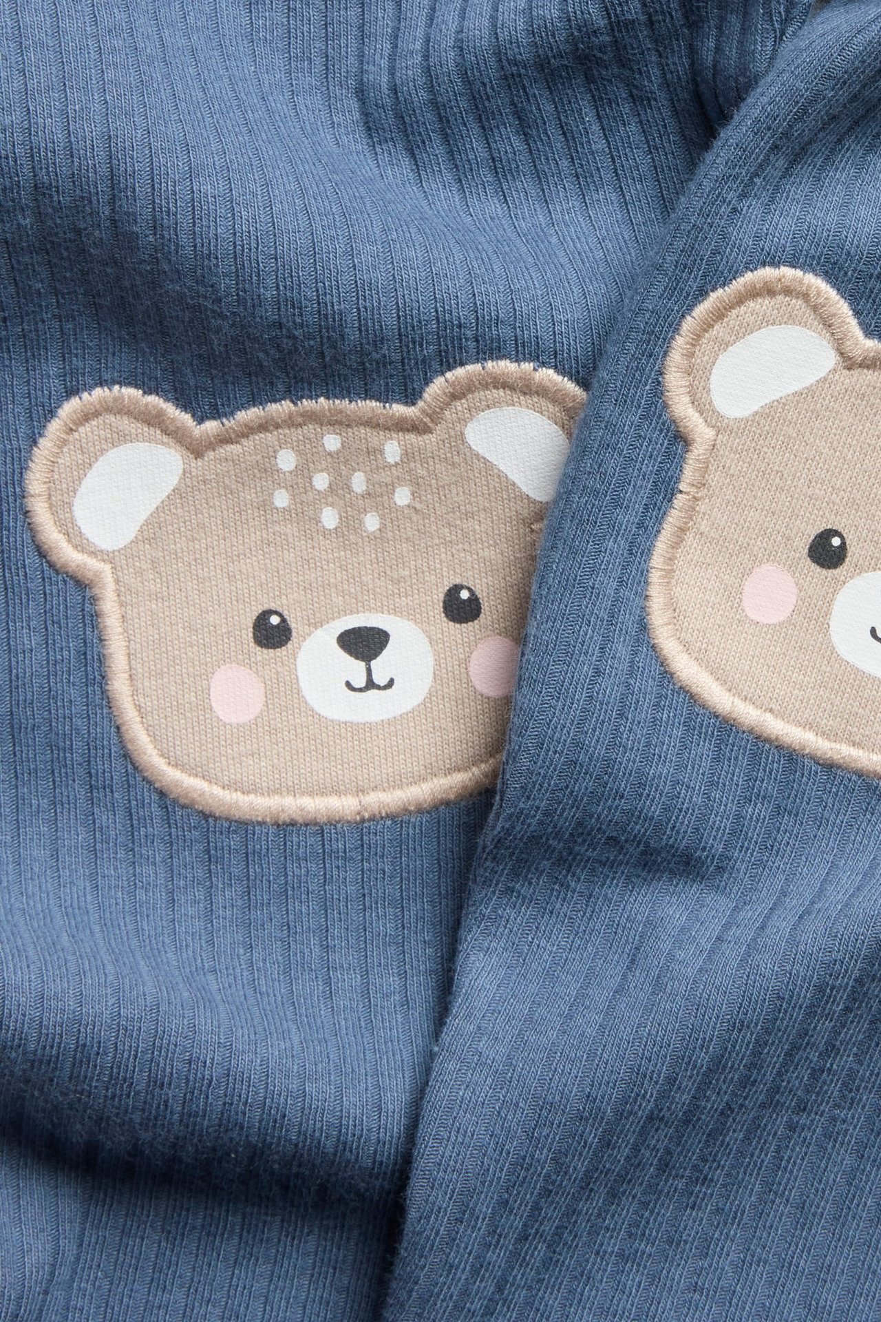 Zbliżenie na niebieskie prążkowane legginsy niemowlęce z jasnobrązowymi aplikacjami misia na kolanach.