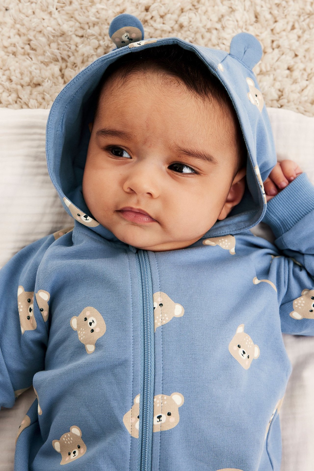 Närbild på baby i ljusblå bomullsjumpsuit med björnmönster, huva med öron och dragkedja.