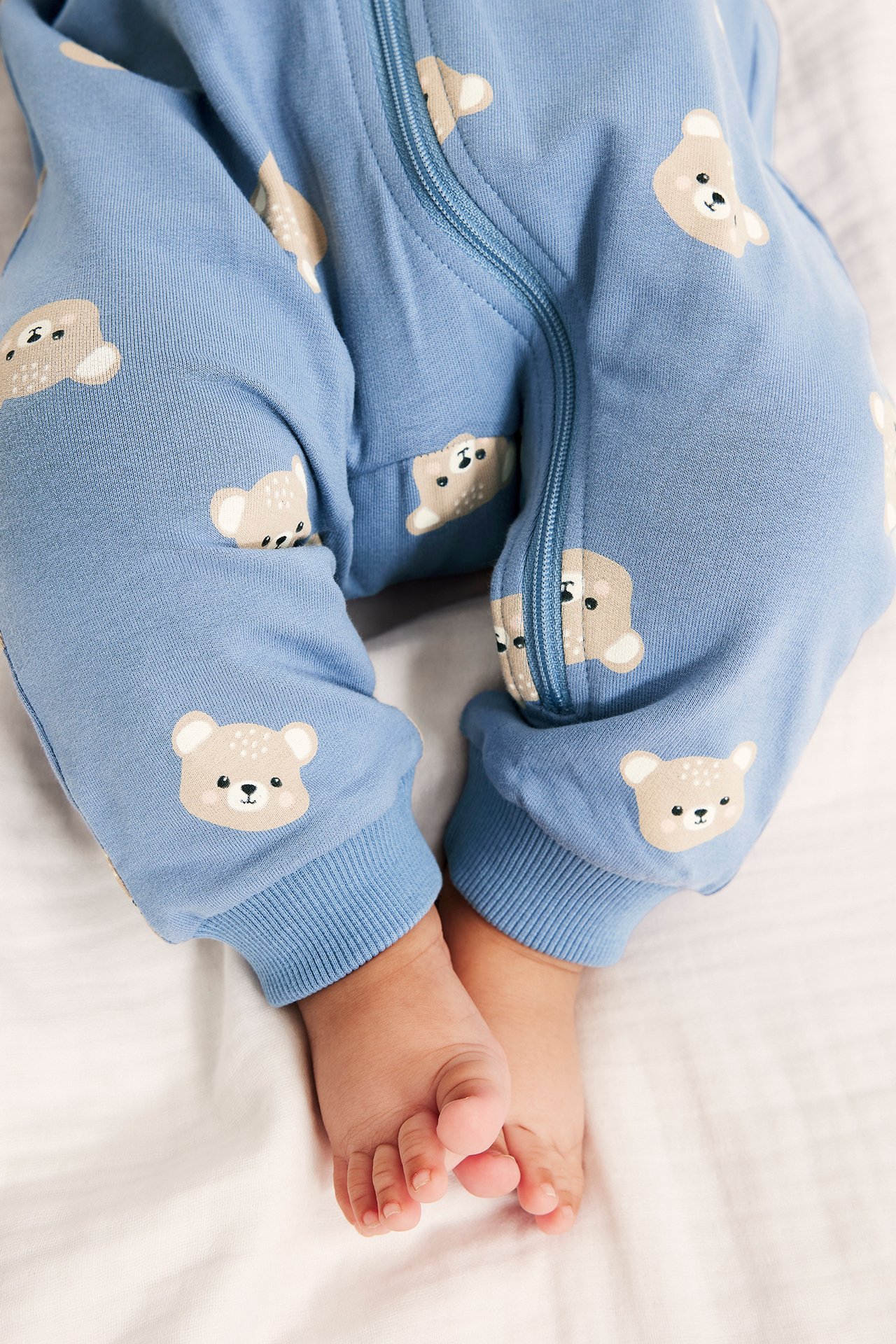 Närbild på baby i ljusblå mönstrad sweatshirt-jumpsuit med björnansikten och dragkedja fram.