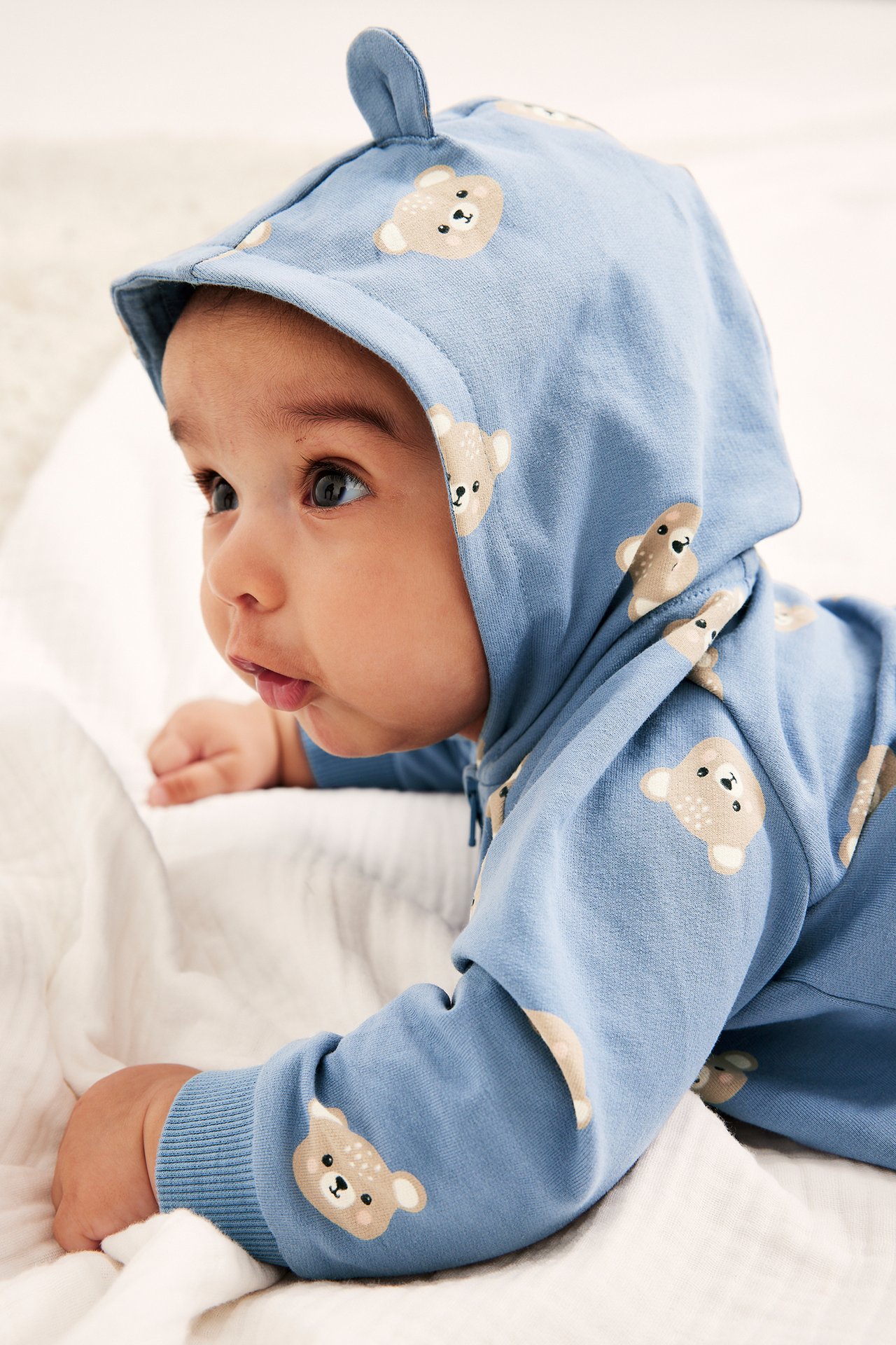 Närbild, sidovy av en baby i en blå björnmönstrad onesie med huva och öron.