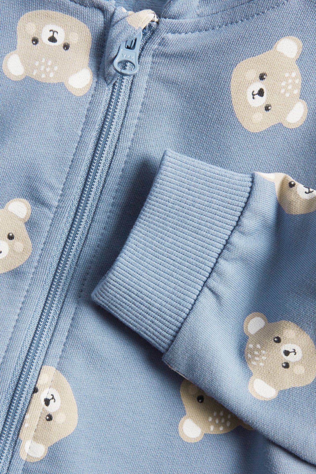 Zbliżenie niebieskiego pajacyka niemowlęcego we wzór misia, z zamkiem błyskawicznym i ściągaczem.