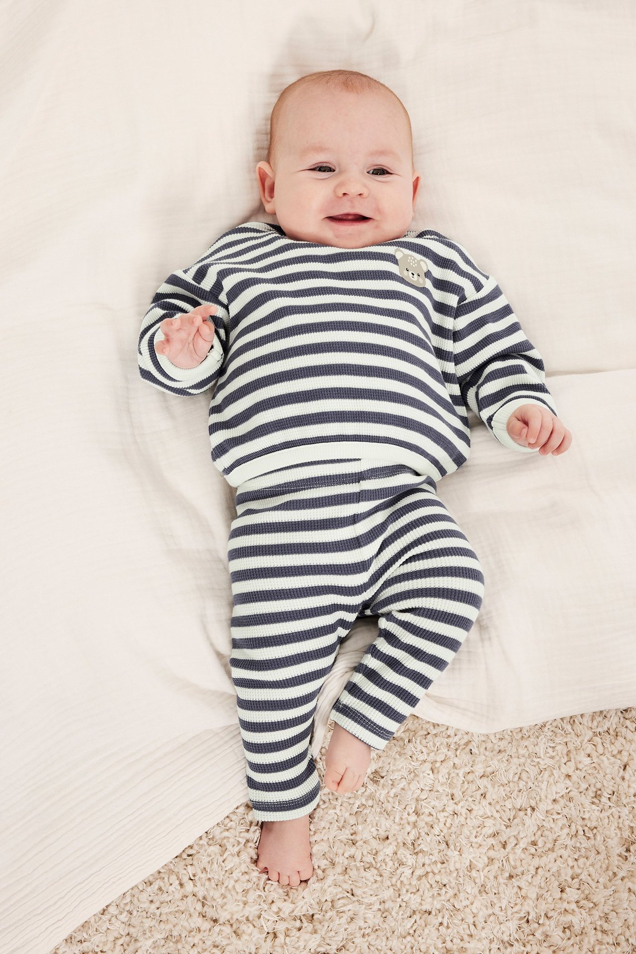 Widok z góry na niemowlę w niebiesko-białych legginsach w paski z dzianiny waflowej i pasującej bluzce.