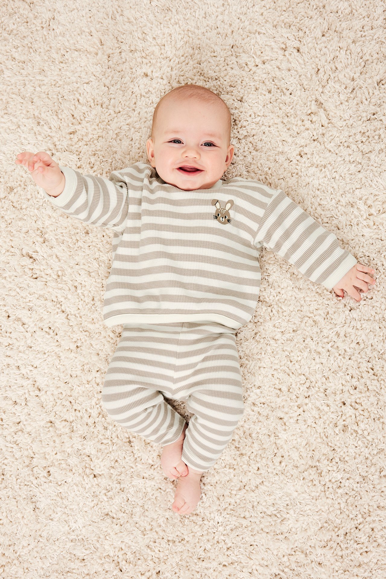 Ovenfra, beige stripete vaffelstrikkede leggings og matchende langermet genser båret av en smilende baby.