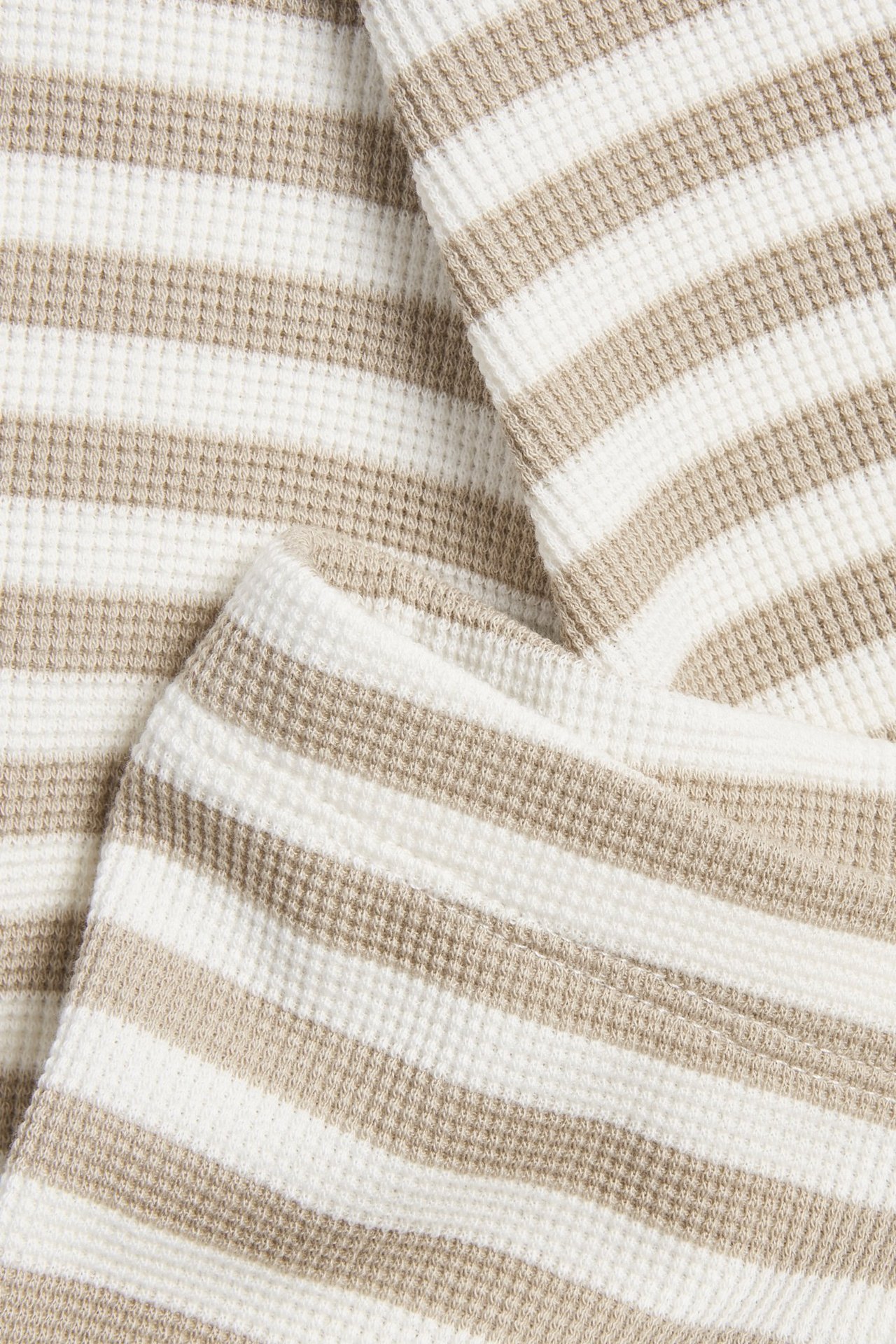 Zbliżenie na beżowo-białe, prążkowane legginsy niemowlęce z dzianiny waflowej.