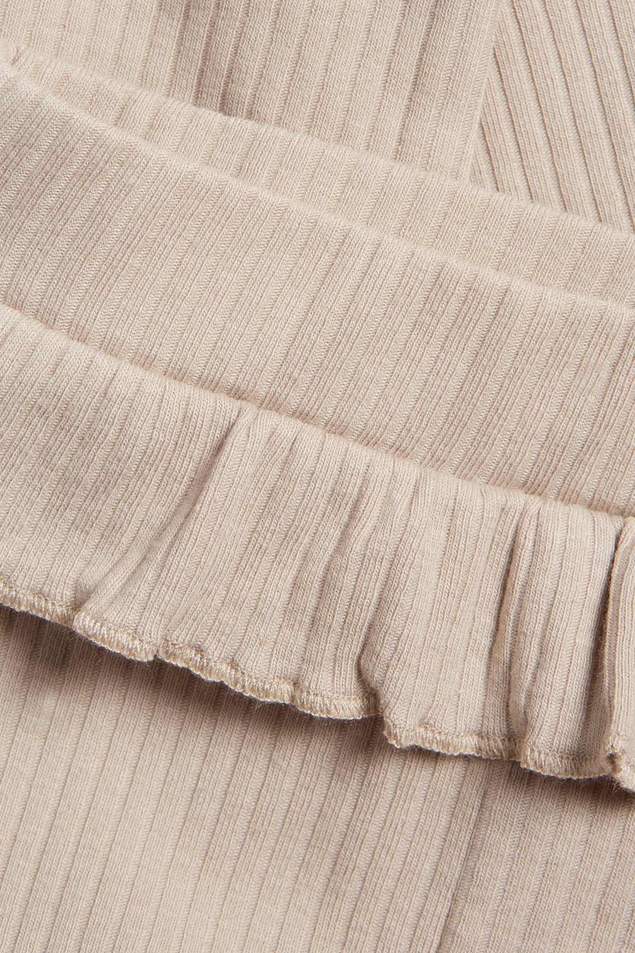 Zbliżenie beżowych, prążkowanych legginsów niemowlęcych z falbanką w pasie.