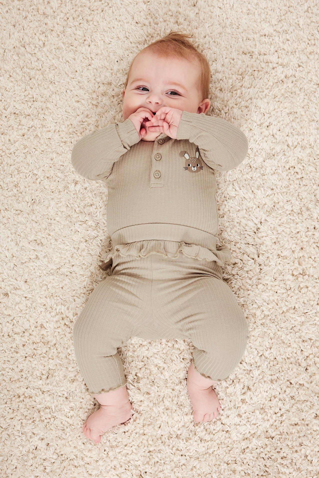 Ovenfra, baby i beige ribbestrikkede leggings med volang i midjen og matchende ribbet topp med kanin.