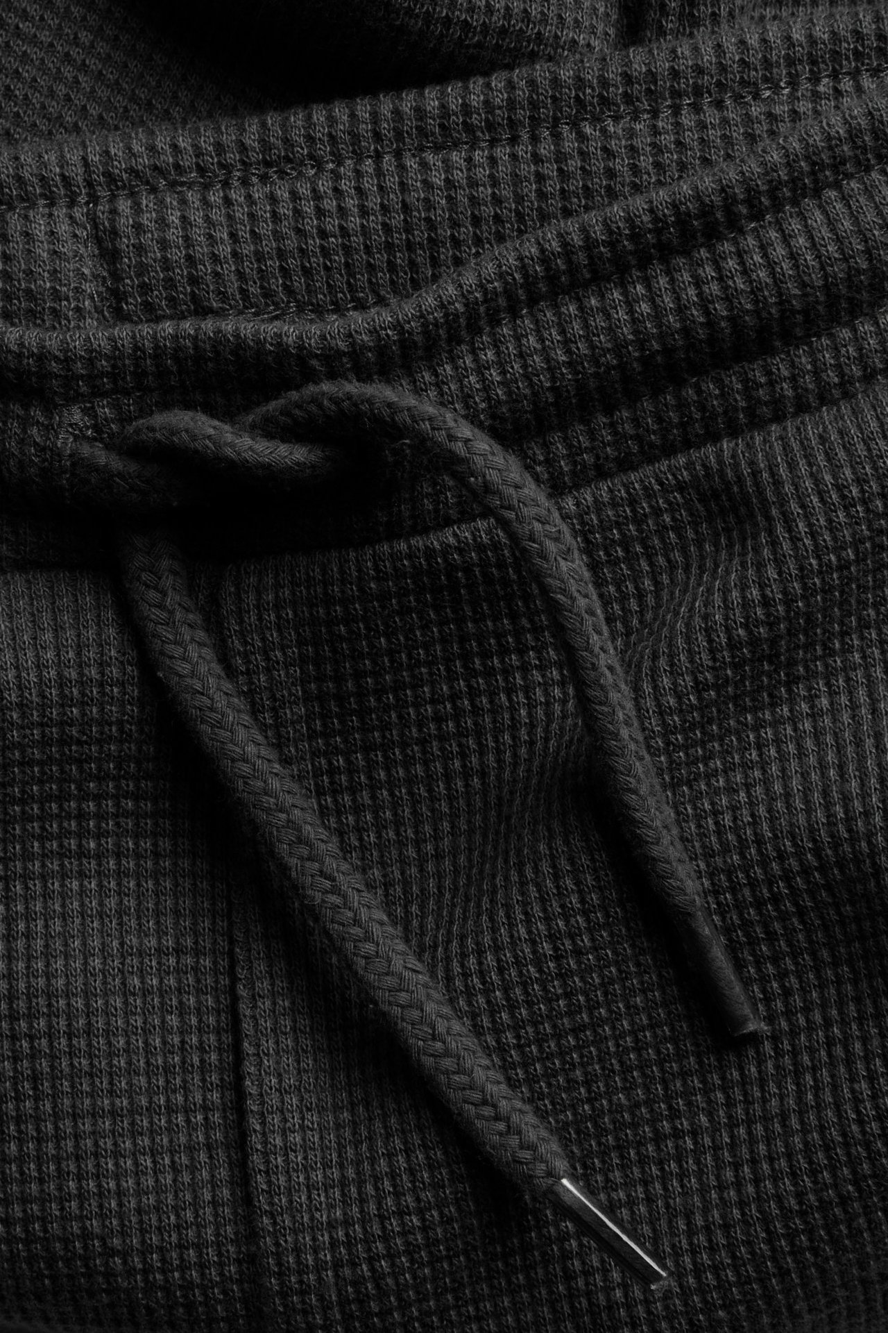 Zbliżenie na czarne bawełniane spodnie waflowe ze sznurkiem w pasie.