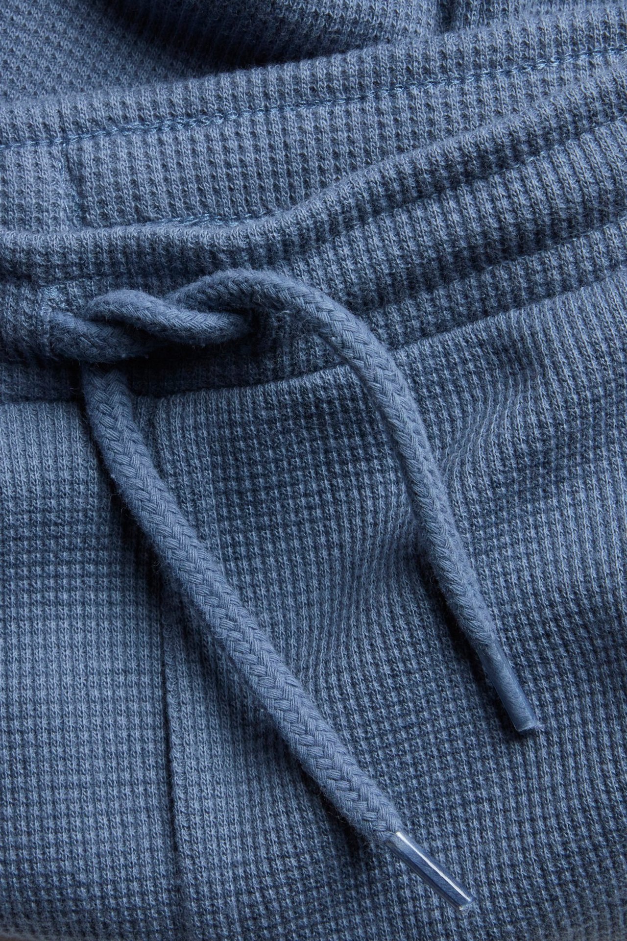 Zbliżenie niebieskich bawełnianych spodni waflowych z wiązanym sznurkiem w pasie.