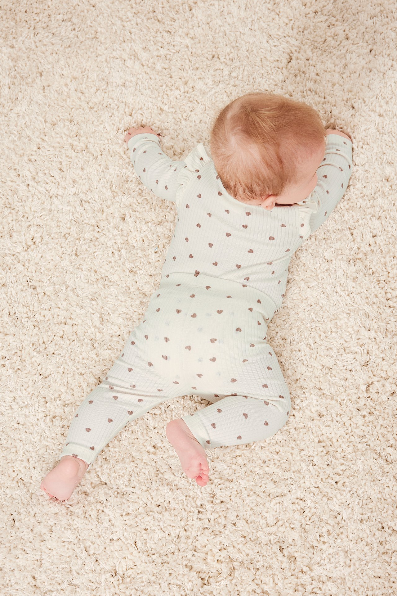 Ylhäältä kuvattu vauva yllään beiget ribatut leggingsit ja yhteensopiva pitkähihainen paita sydänkuviolla.
