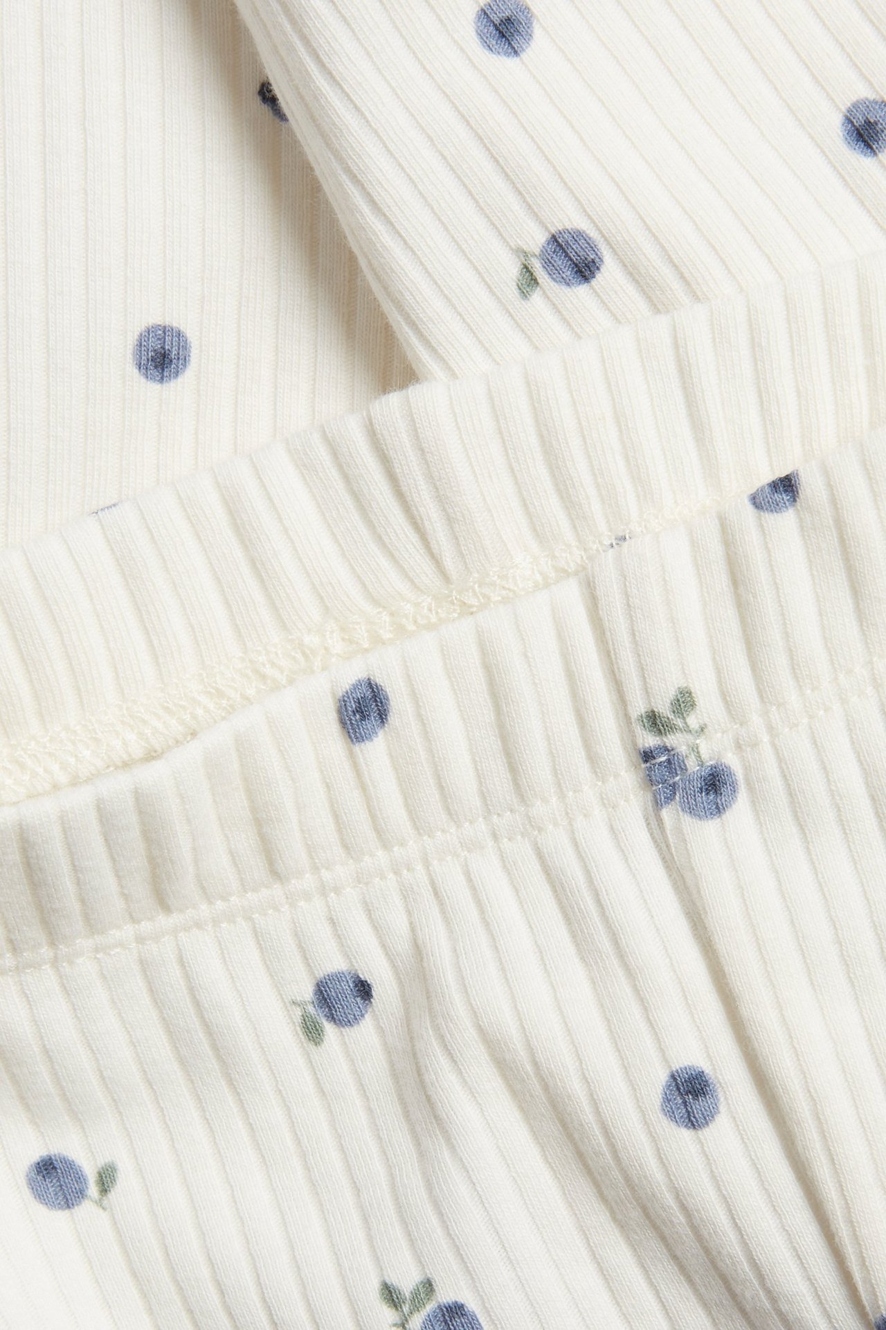 Zbliżenie na kremowe prążkowane legginsy niemowlęce z niebieskim wzorem jagód i elastyczną talią.