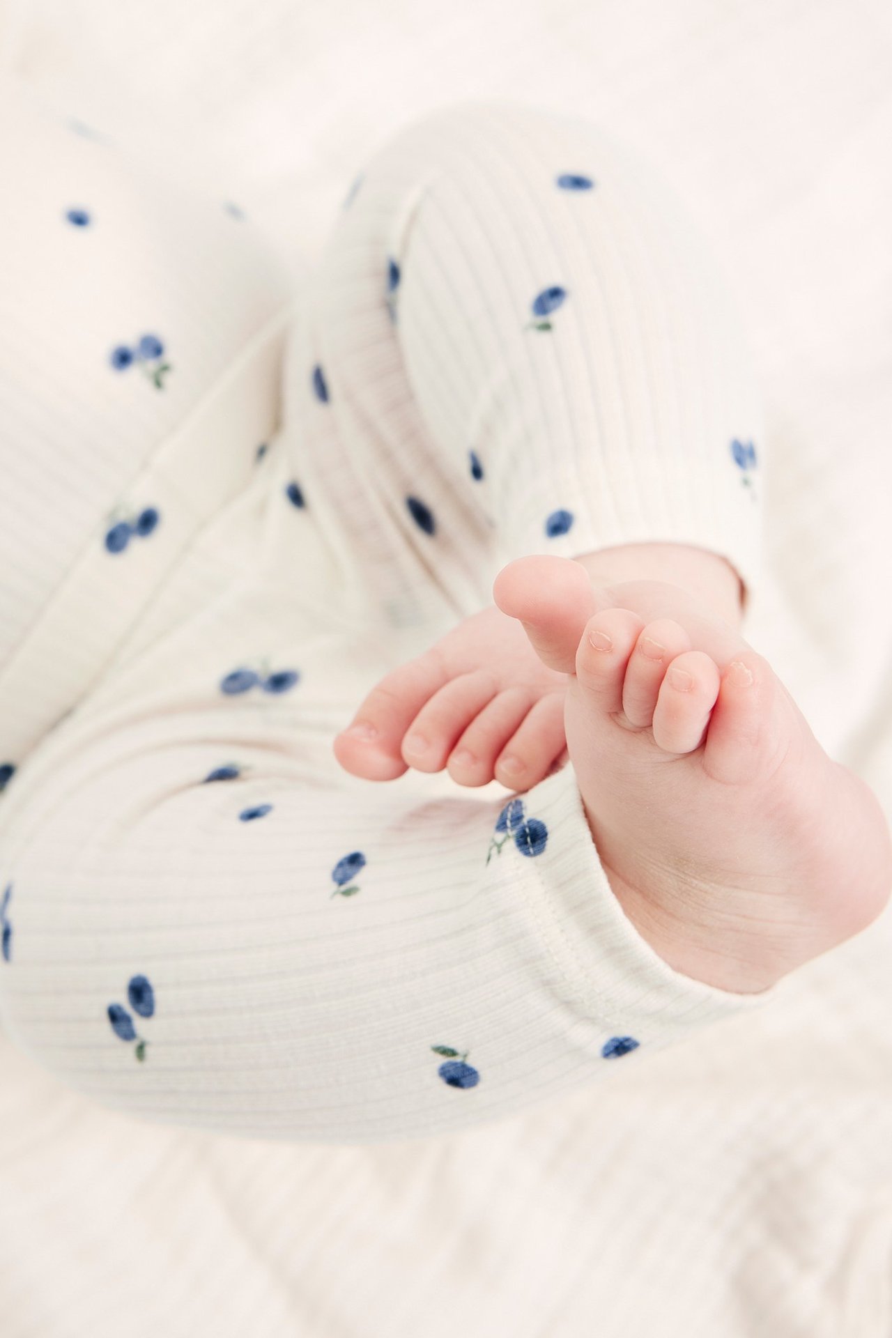 Nærbilde av baby i offwhite ribbestrikkede leggings med blått blåbærmønster.