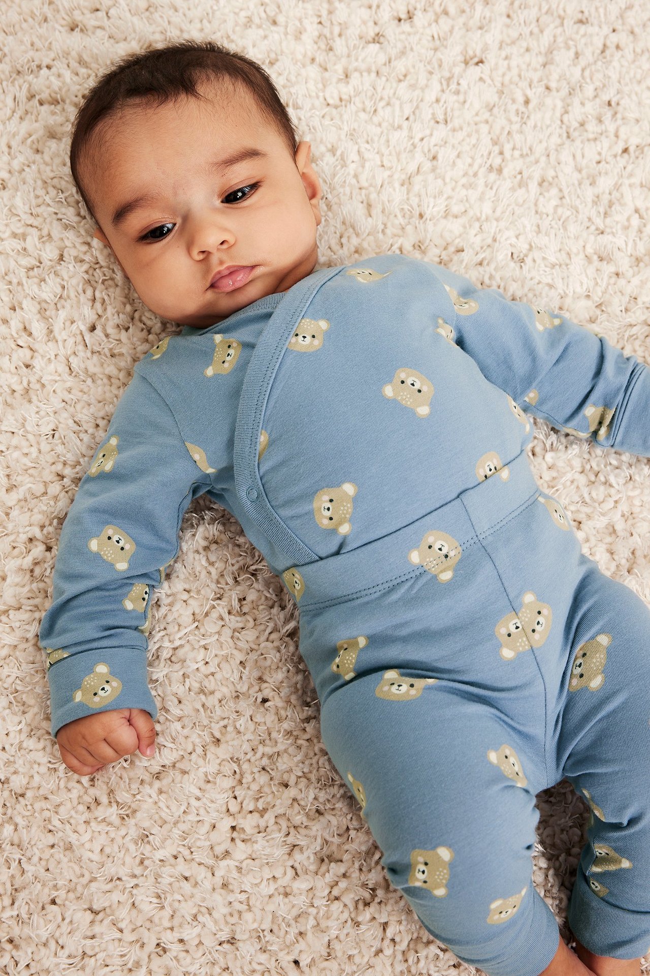 Ovenfra-bilde av en baby i en blå mønstret body med bjørneansikter og overlappende front.
