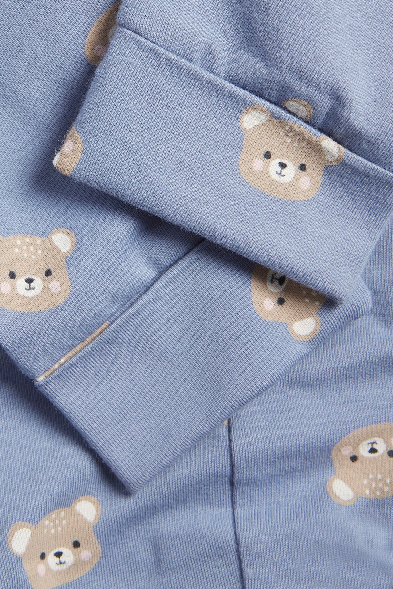 Zbliżenie na niebieskie legginsy niemowlęce z uroczym wzorem misia i podwiniętymi mankietami.