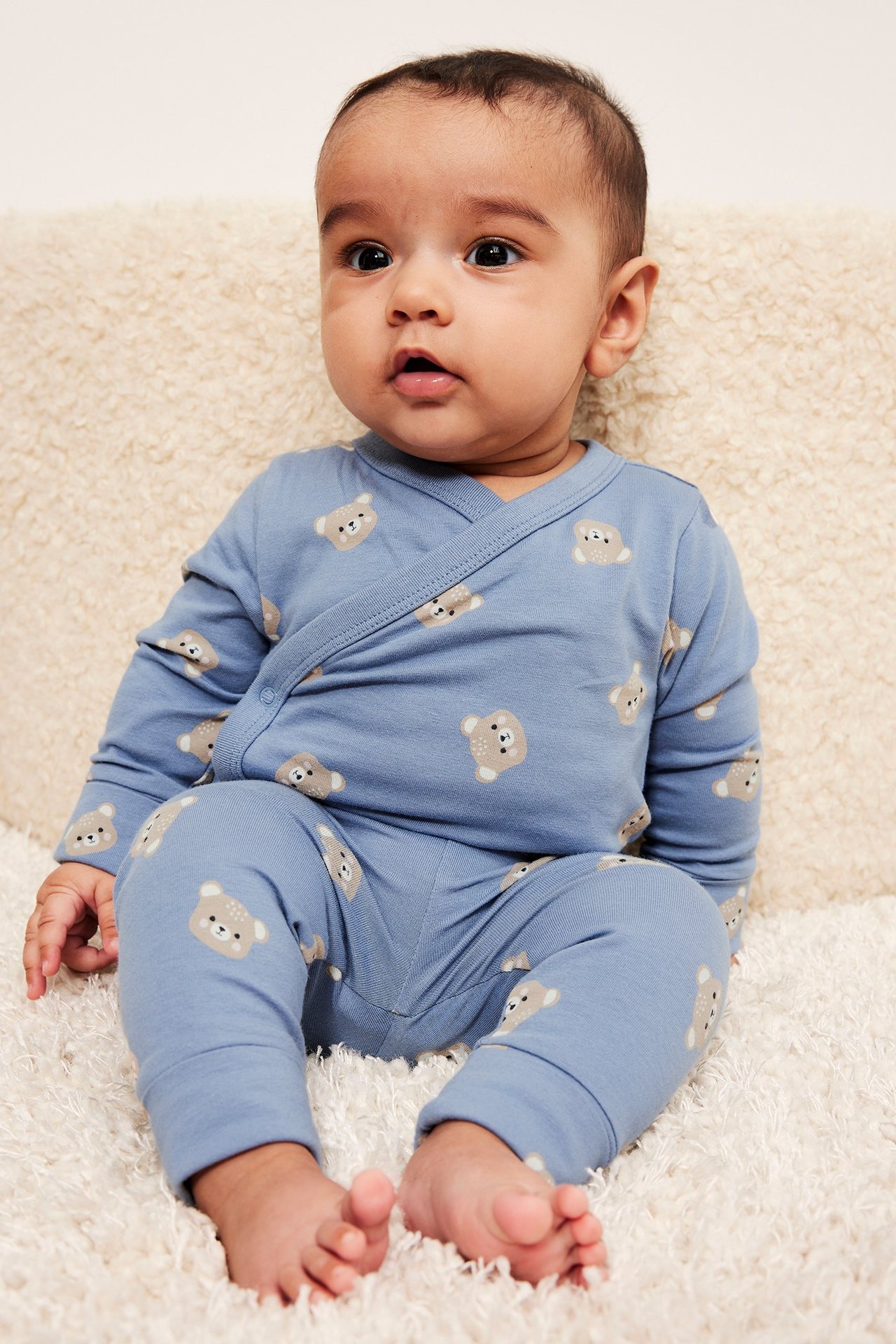 Edestäpäin kuvattu vauva yllään siniset kuviolliset leggingsit karhun kasvoilla ja yhteensopiva kietaisupaita.