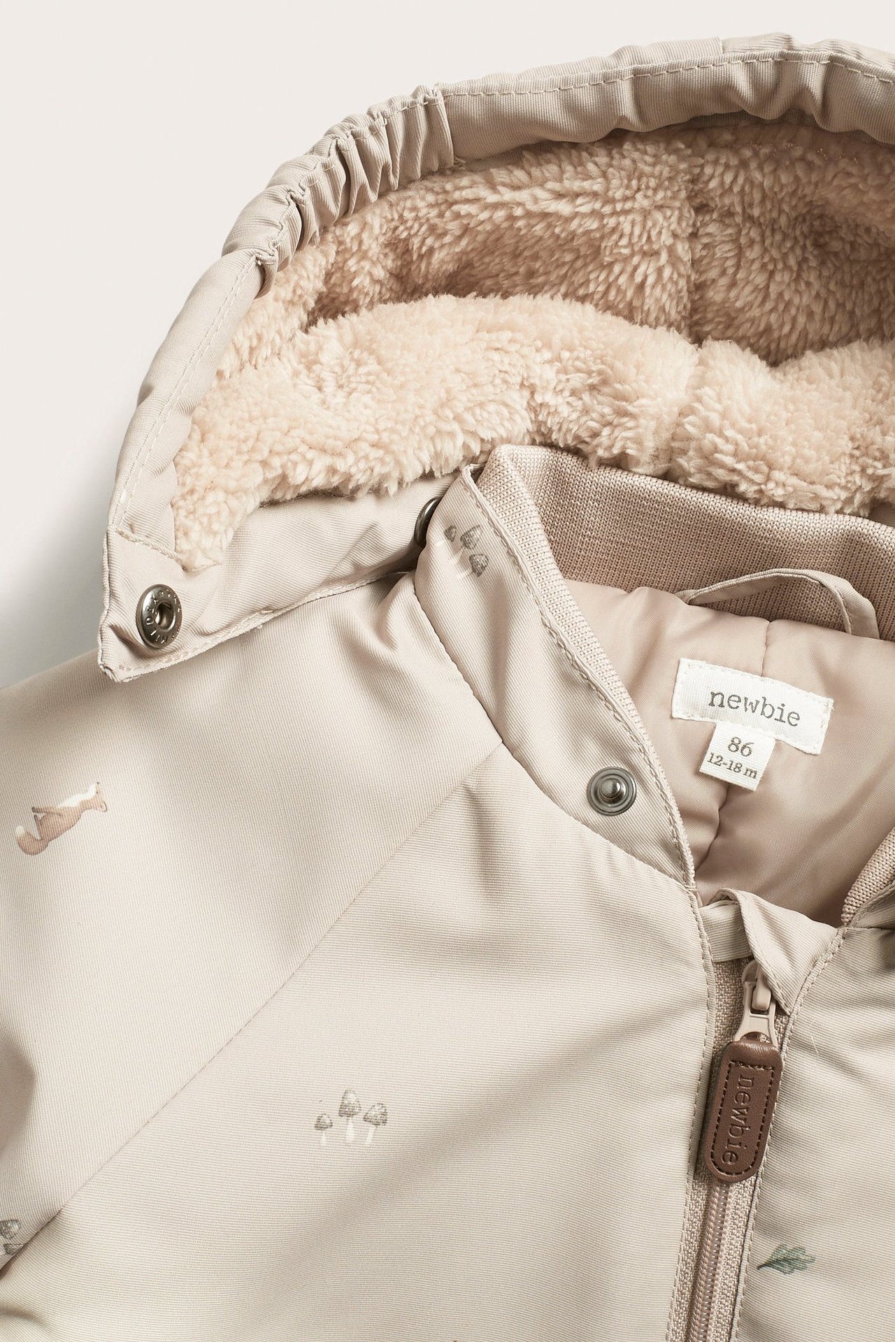 Zbliżenie beżowego wiatroodpornego kombinezonu niemowlęcego z lisami i grzybami, z puszystą podszewką kaptura.