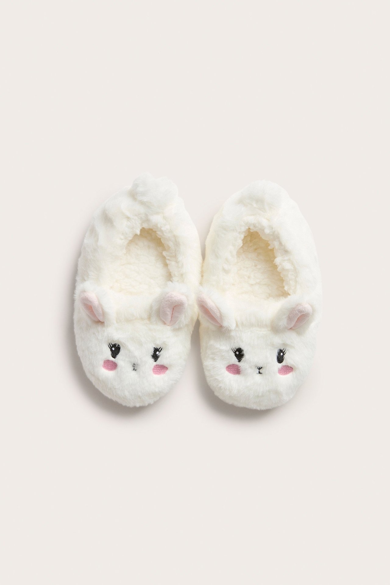 Ylhäältä kuvatut luonnonvalkoiset tekoturkiskaninitossut, joissa on brodeeratut kasvot ja korvat.