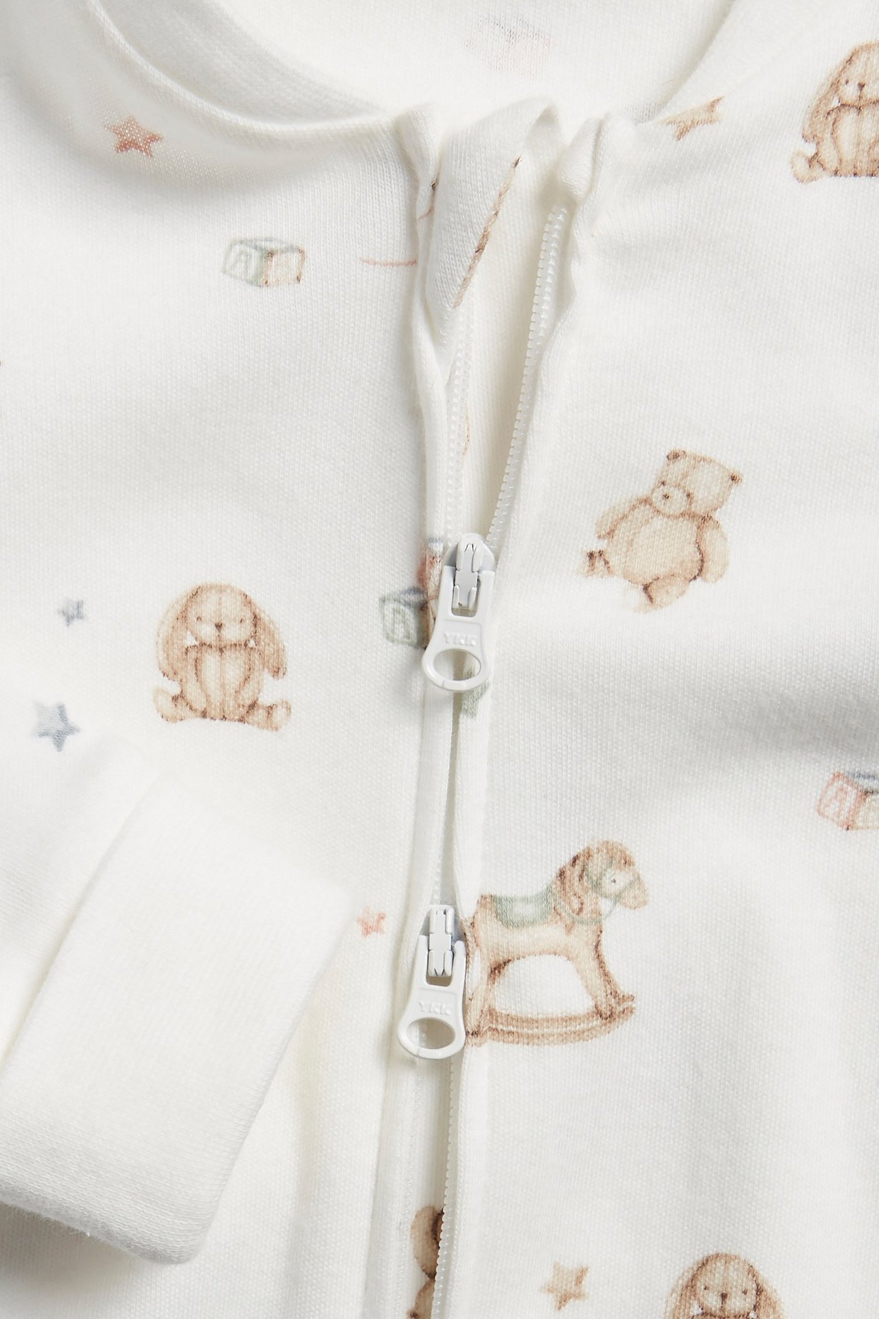 Närbild på en offwhite babypyjamas med leksaksmönster och tvåvägsdragkedja.