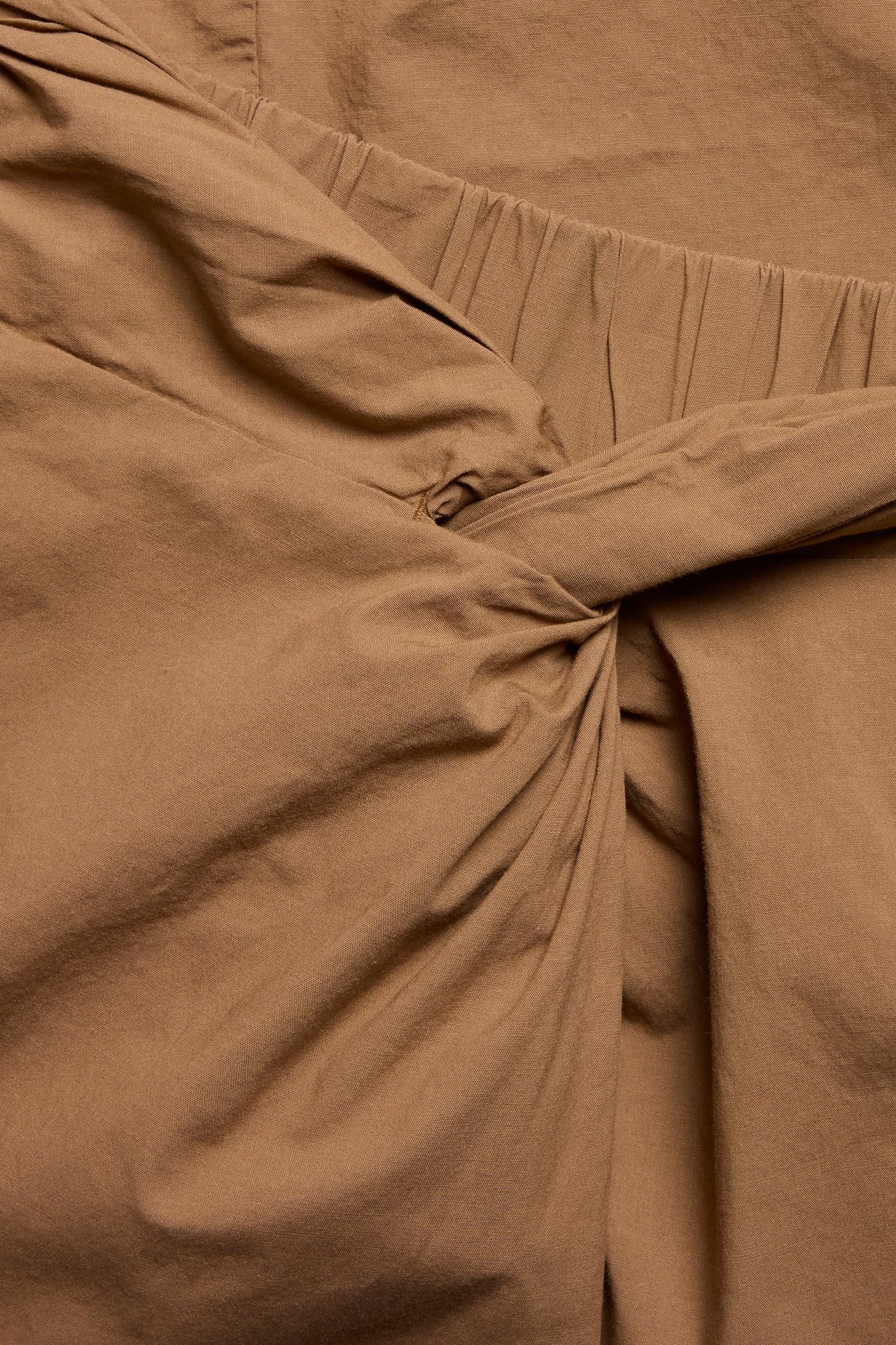 Zbliżenie brązowej spódnicy midi z mieszanki bawełny, z węzłem i drapowaniem z przodu oraz elastyczną talią.