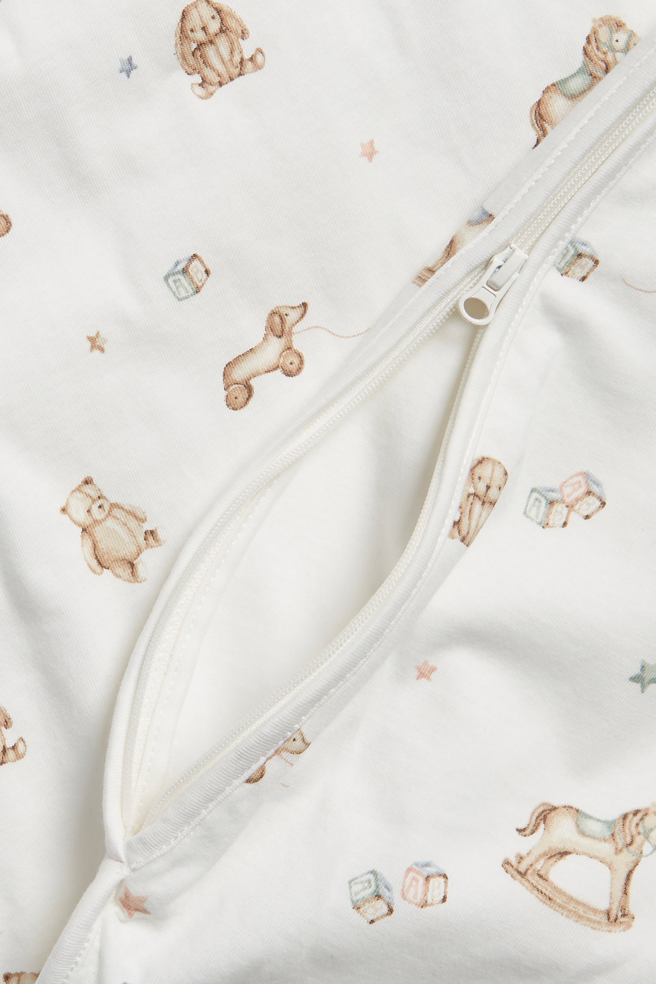 Närbild på en offwhite babynattpåse med leksaksmönster och en delvis öppen vit dragkedja.